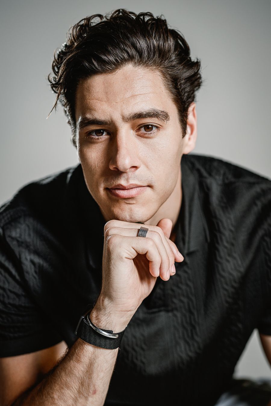 Studio portrait with dramatic lighting against grey background wearing black shirt.