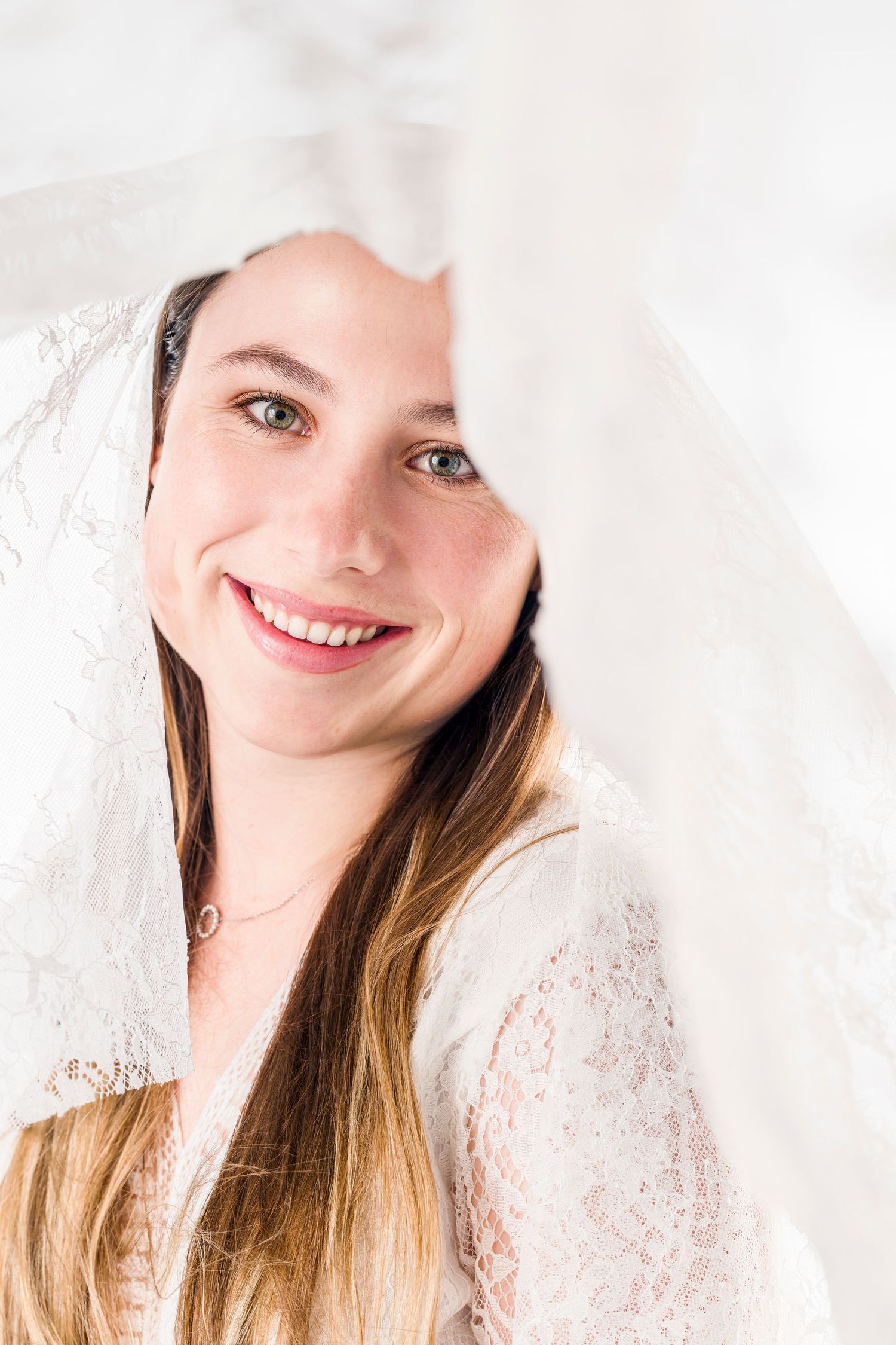 Joyful bridal portrait peeking through white lace veil.