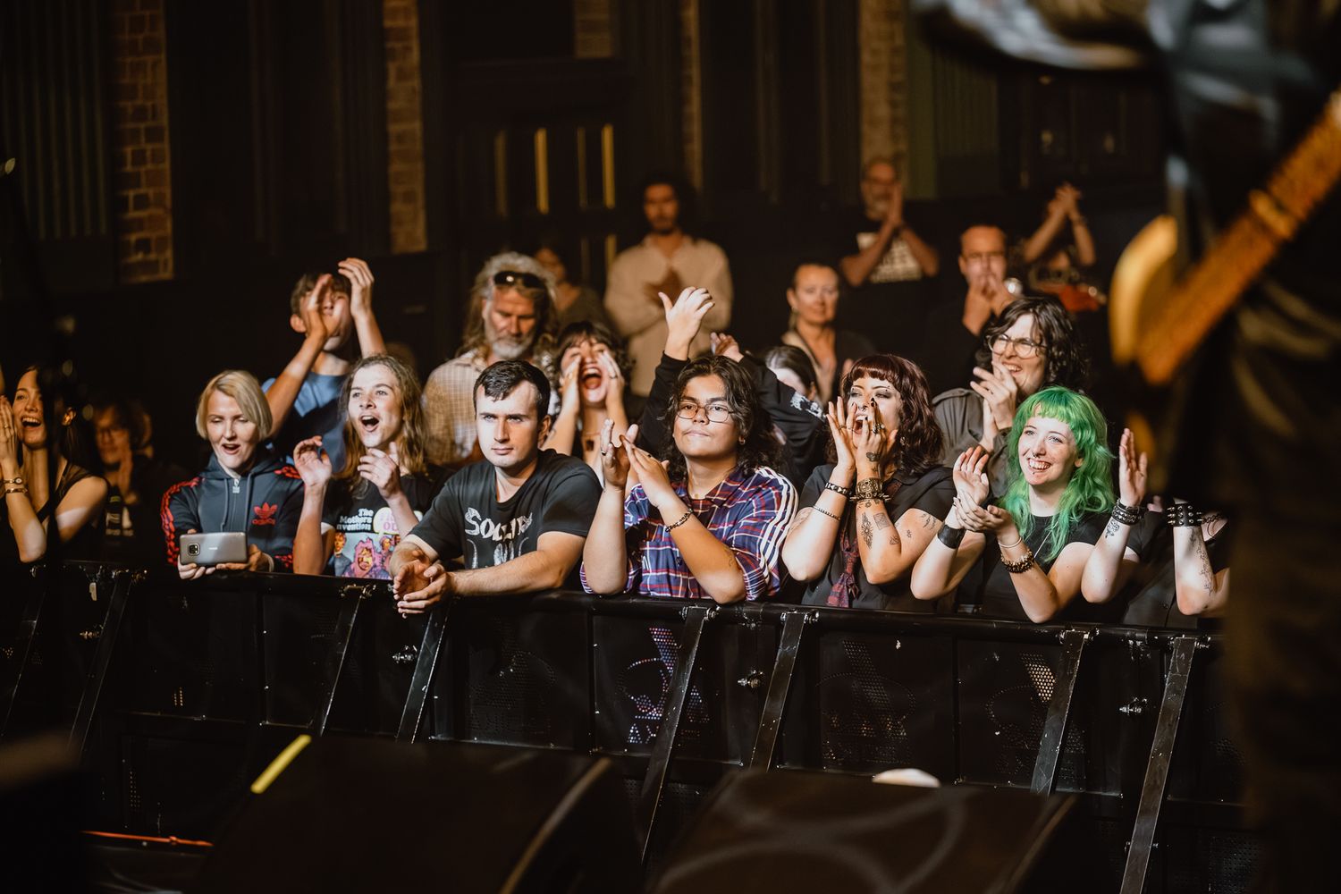 Concert audience watching performance with enthusiastic expressions and raised hands.