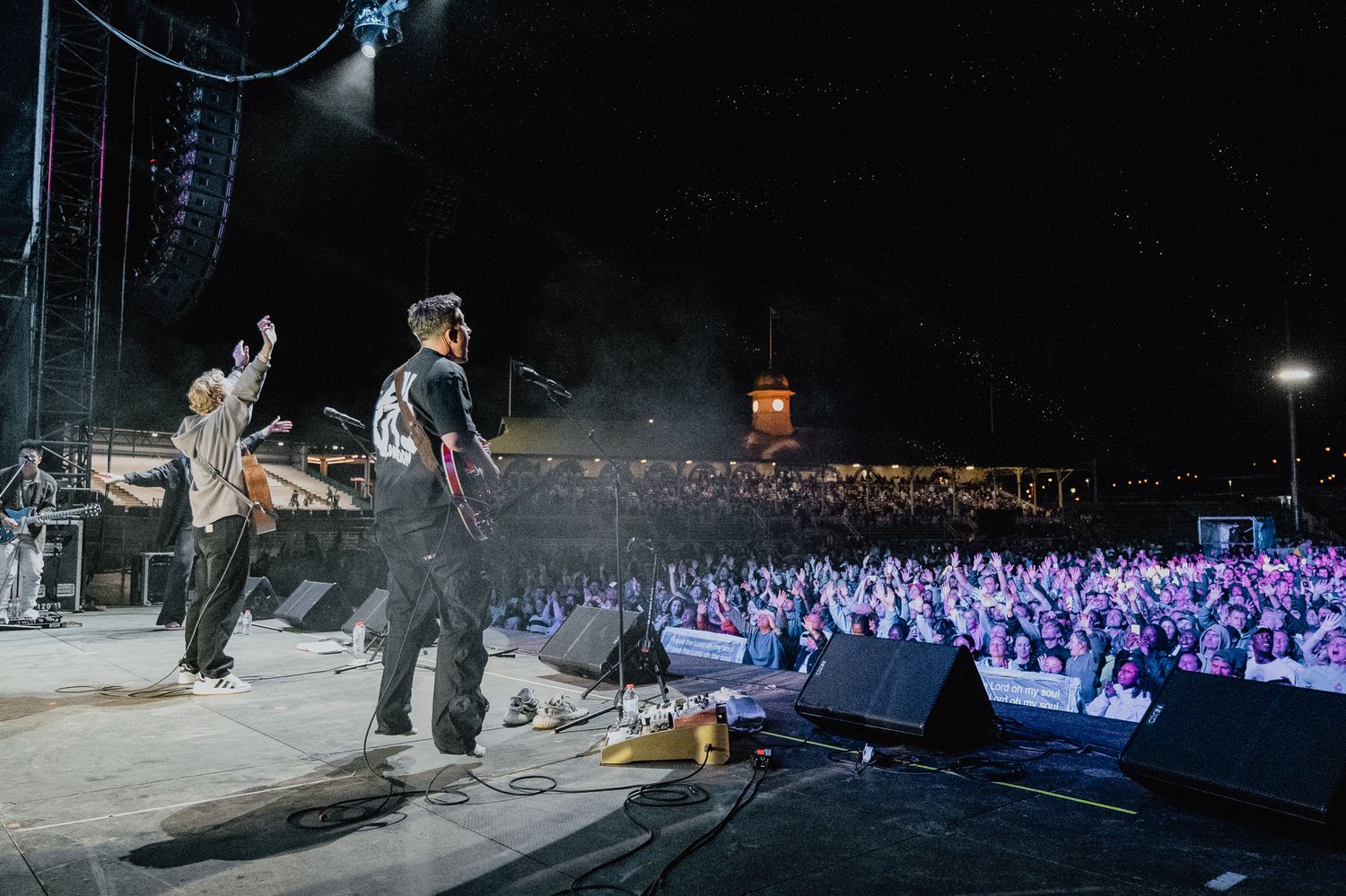 Wide shot of concert stage with dramatic lighting and large audience in view.