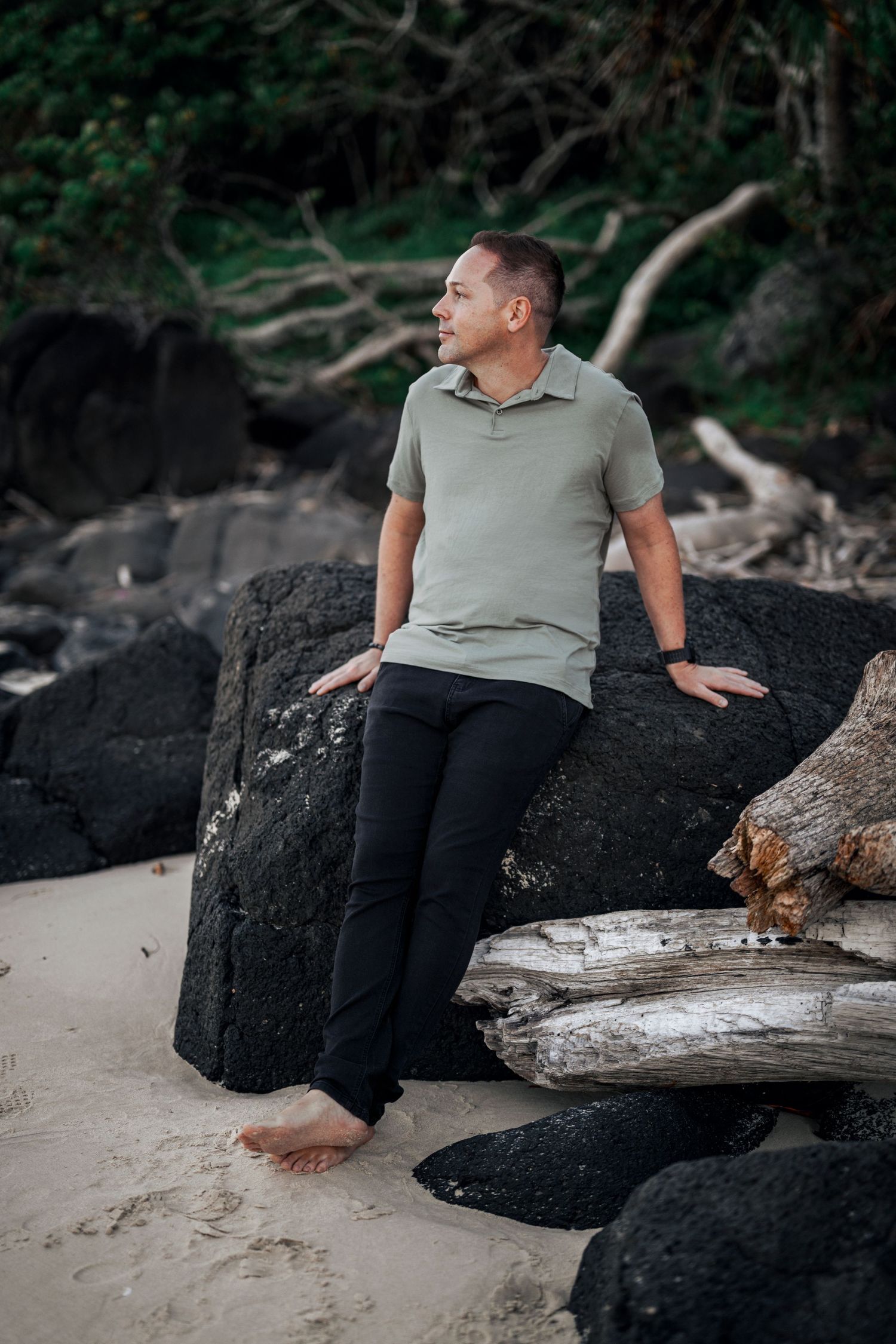 Person relaxing on driftwood and rocks at a moody beach setting.
