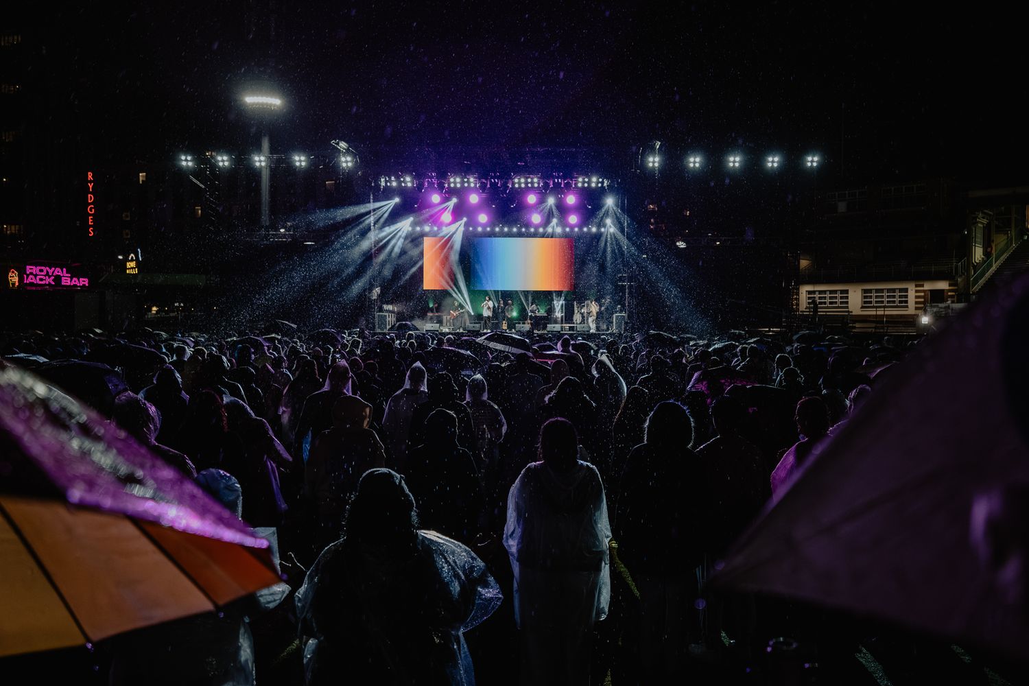 Concert venue at night with silhouetted crowd and colorful stage lighting.