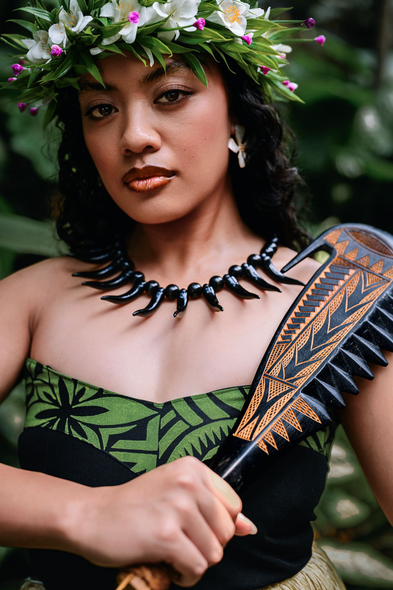 Polynesian woman in floral crown, black tooth necklace, green tropical dress, holding carved wooden paddle.