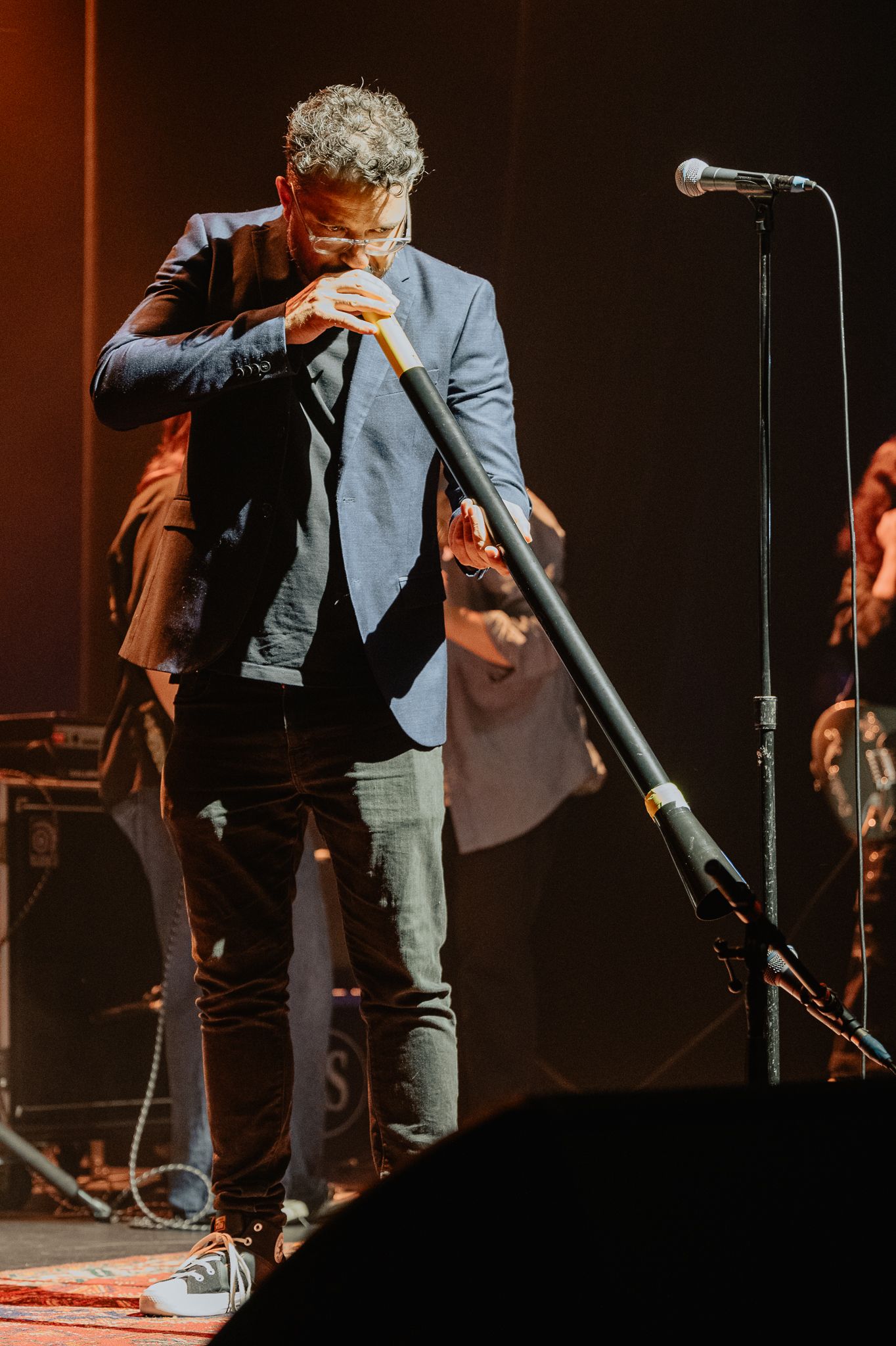 Performer in a suit jacket singing into microphone on dimly lit stage.