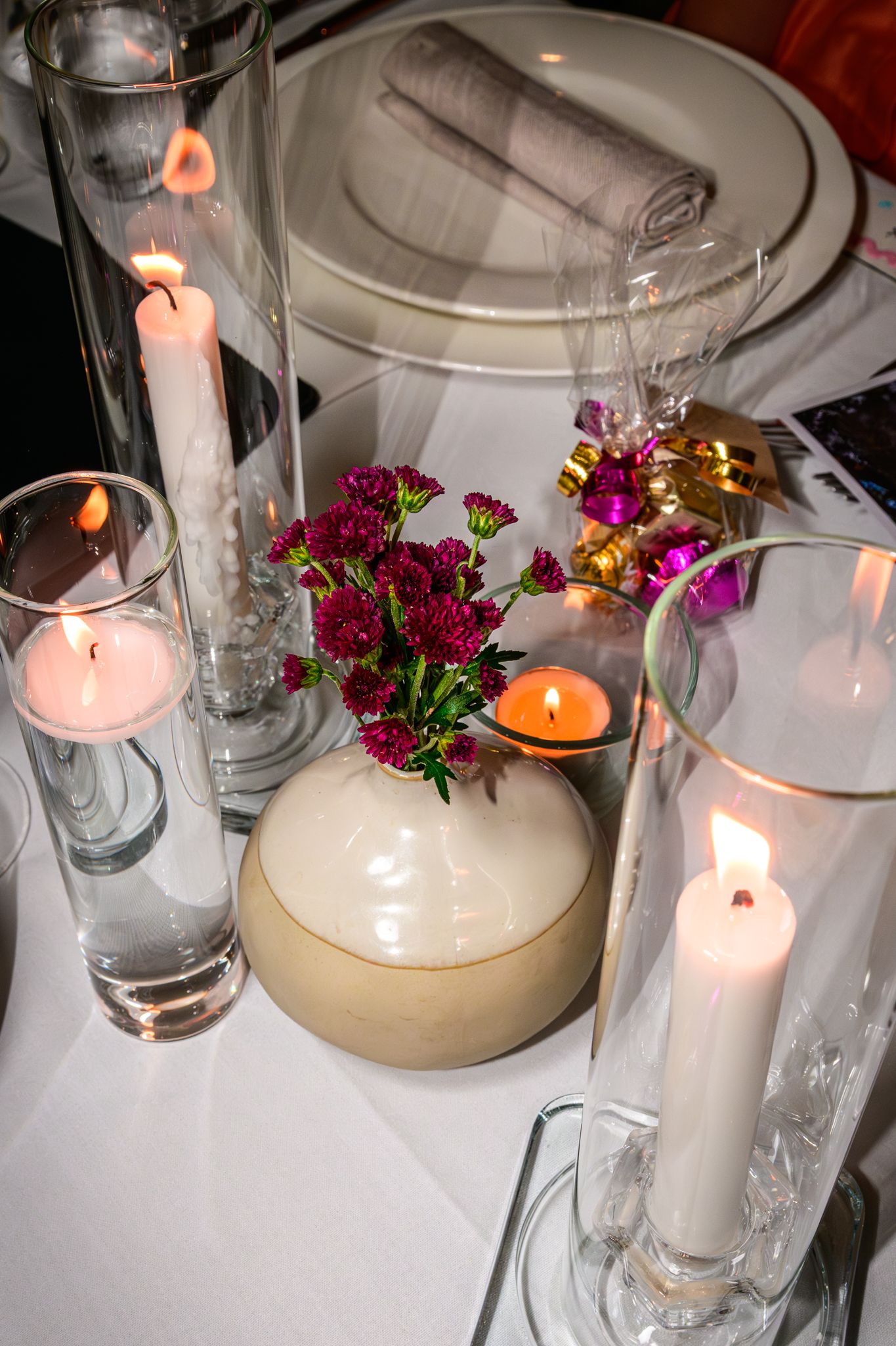 Elegant table setting with lit candles and purple flowers in glass vases.