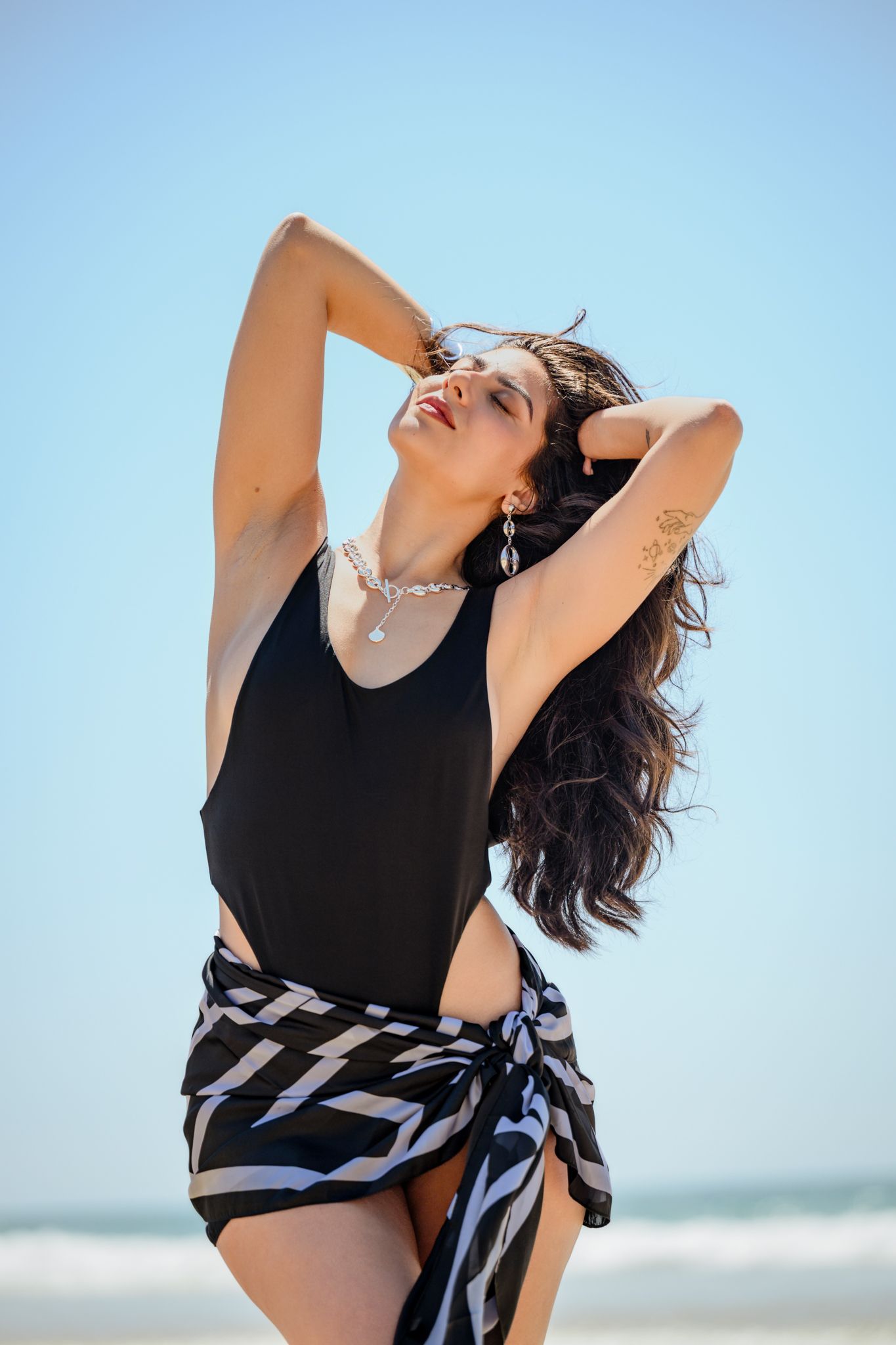 Beach fashion photography with flowing fabric and movement against bright blue sky.
