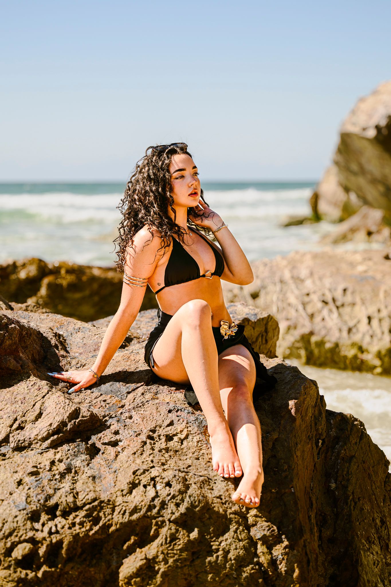 Model lounging on rocky beach formation during golden hour photoshoot.