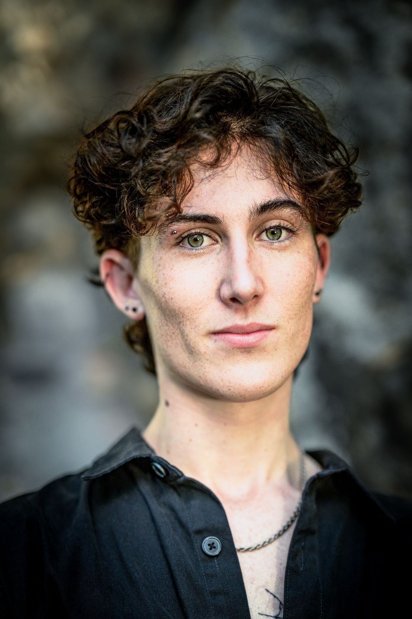 Close-up portrait against blurred background showing curly dark hair and black shirt.