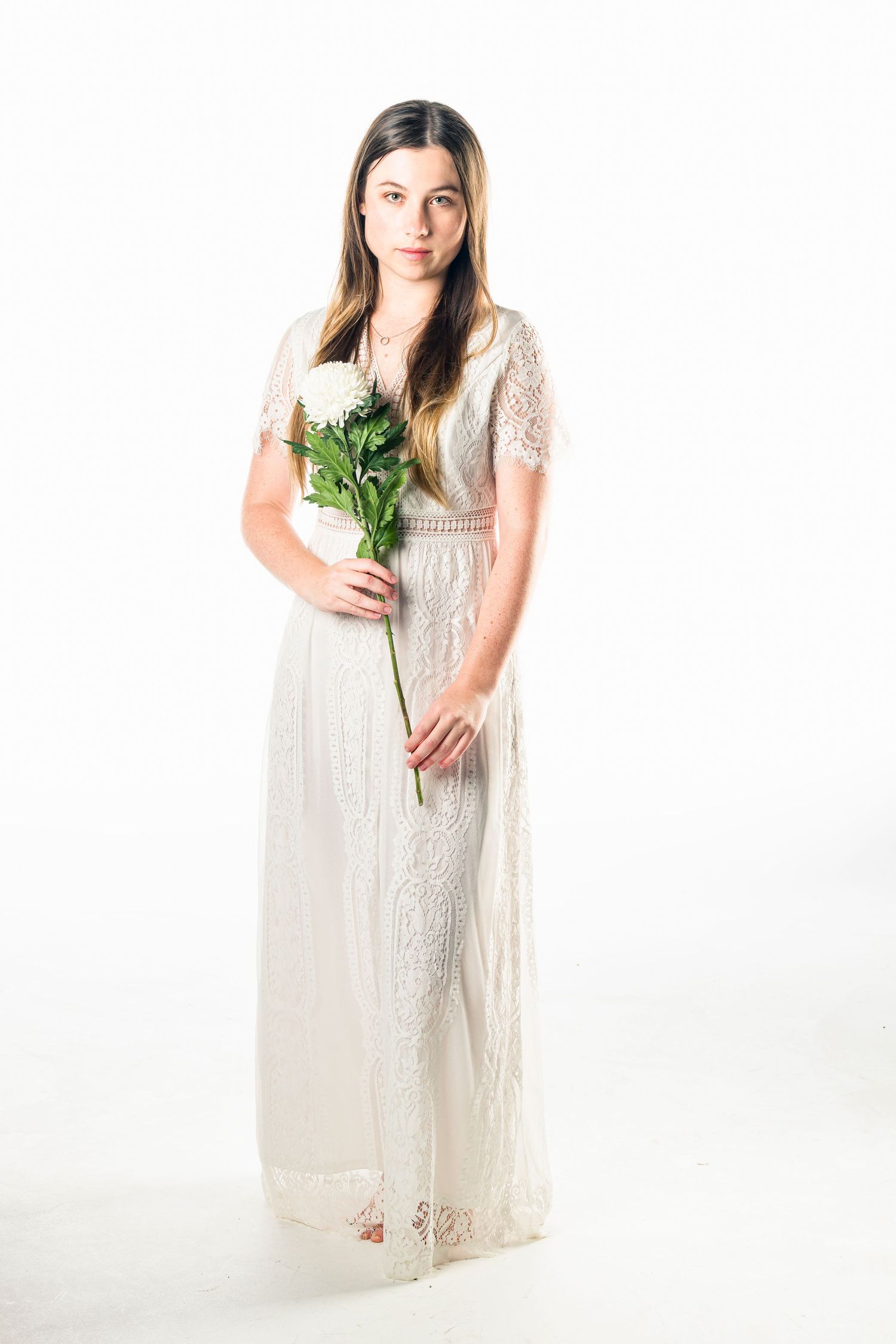 Full length portrait in white lace dress holding flowers against white background.