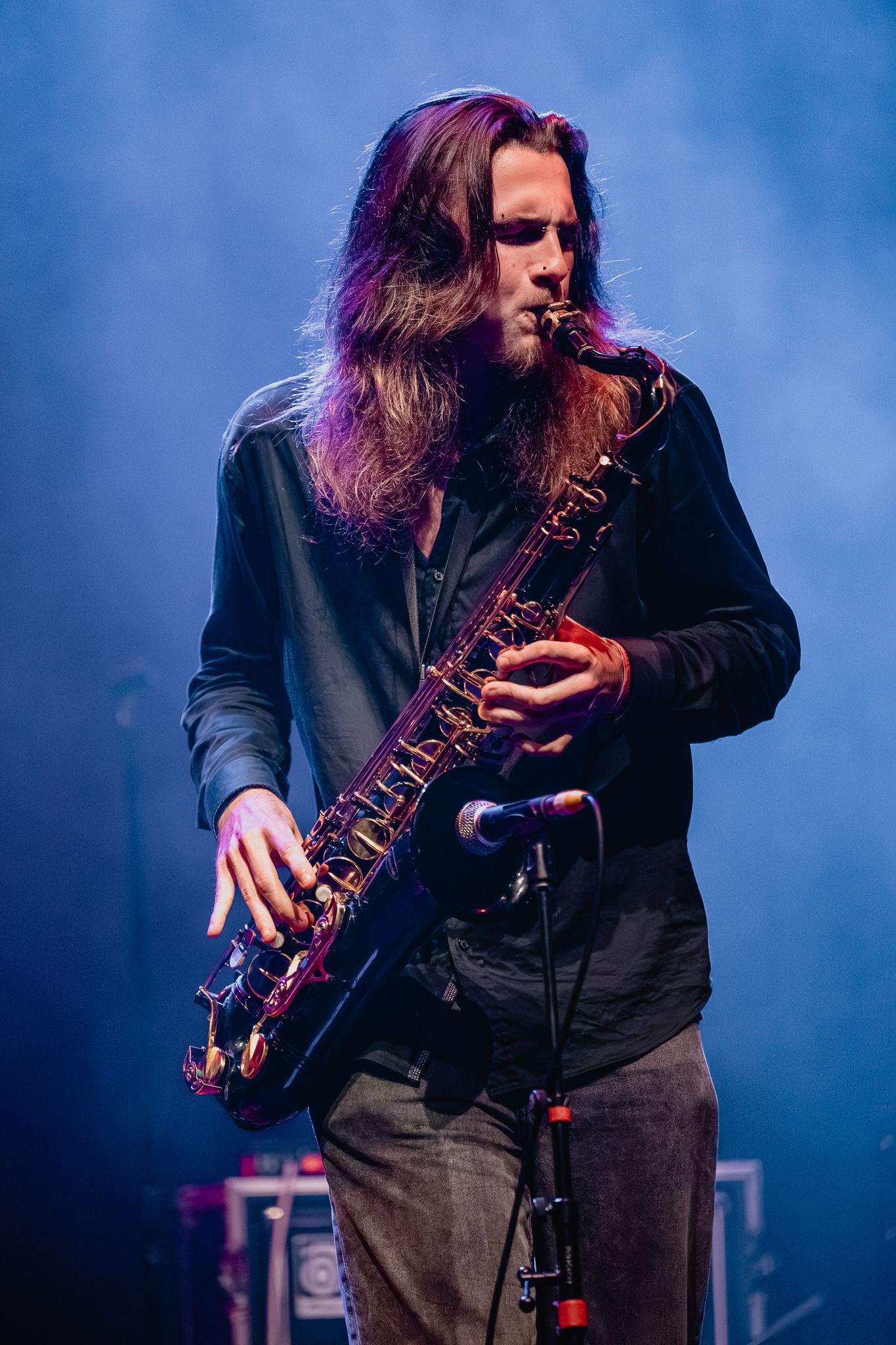 Musician playing saxophone on stage illuminated by blue and purple stage lights.