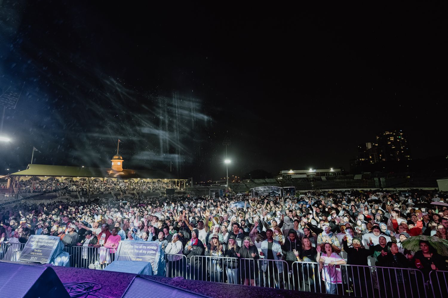 Panoramic view of large outdoor nighttime event with crowd and stage lighting.