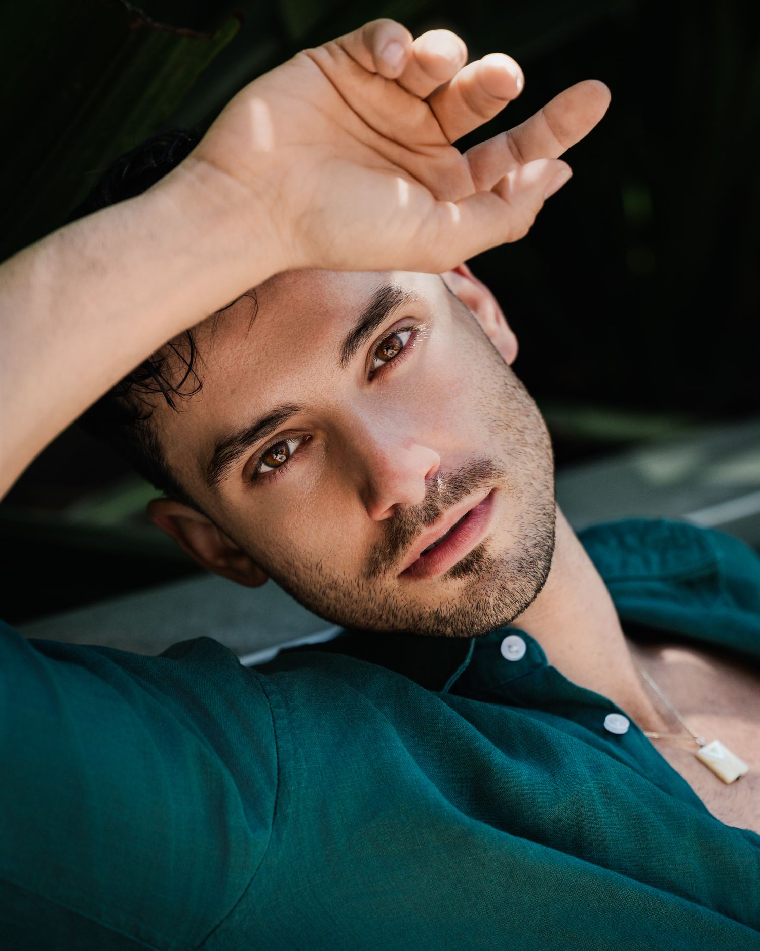 Artistic portrait in dark teal tones showing relaxed pose against dark background.