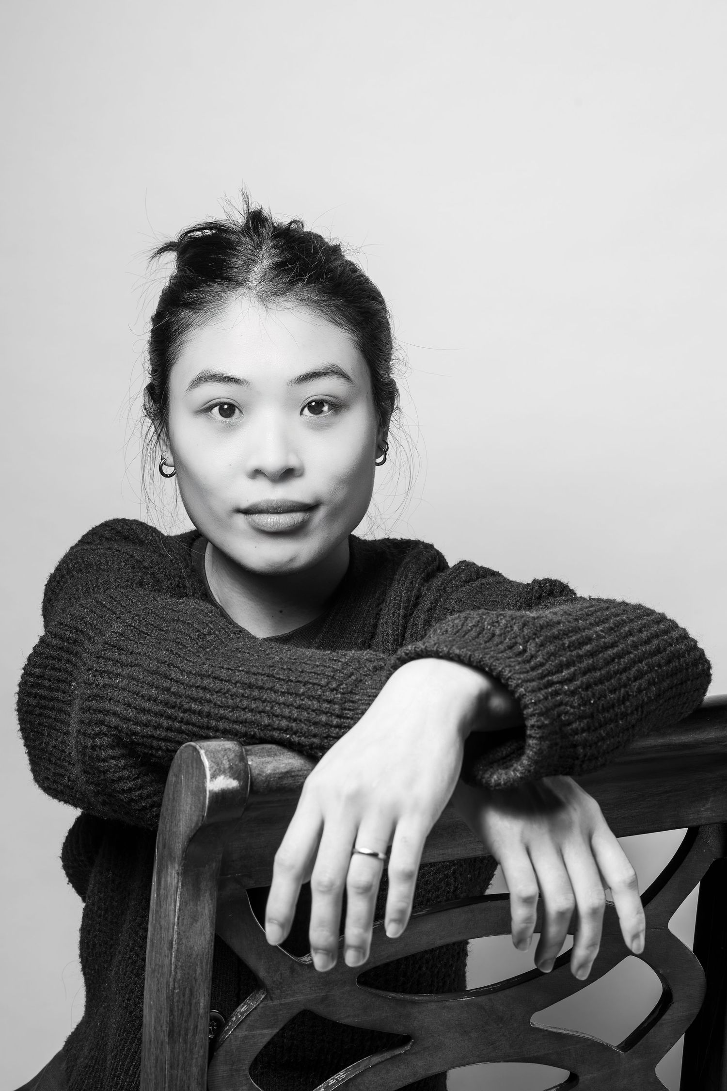 Black and white portrait of a person in sweater leaning on wooden chair.