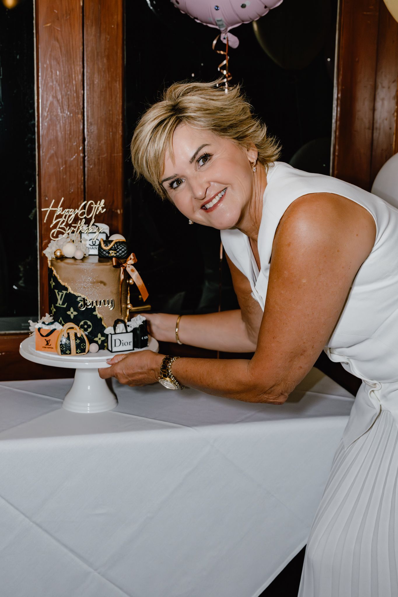 Woman in white dress cutting a decorated celebration cake at an event.