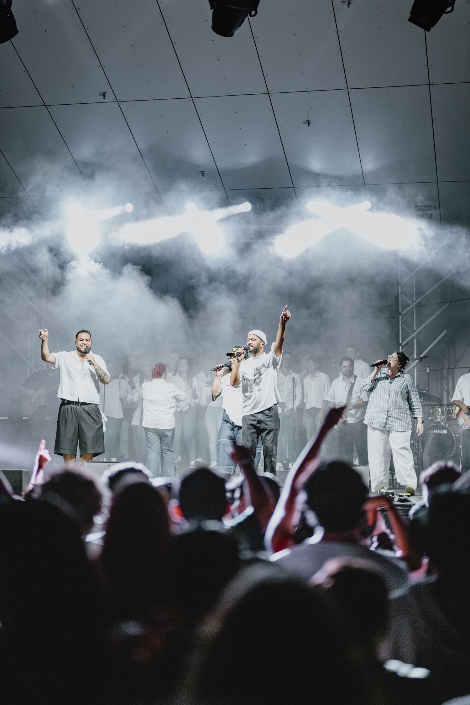 Performers on stage with dramatic fog effects and silhouetted crowd in foreground.