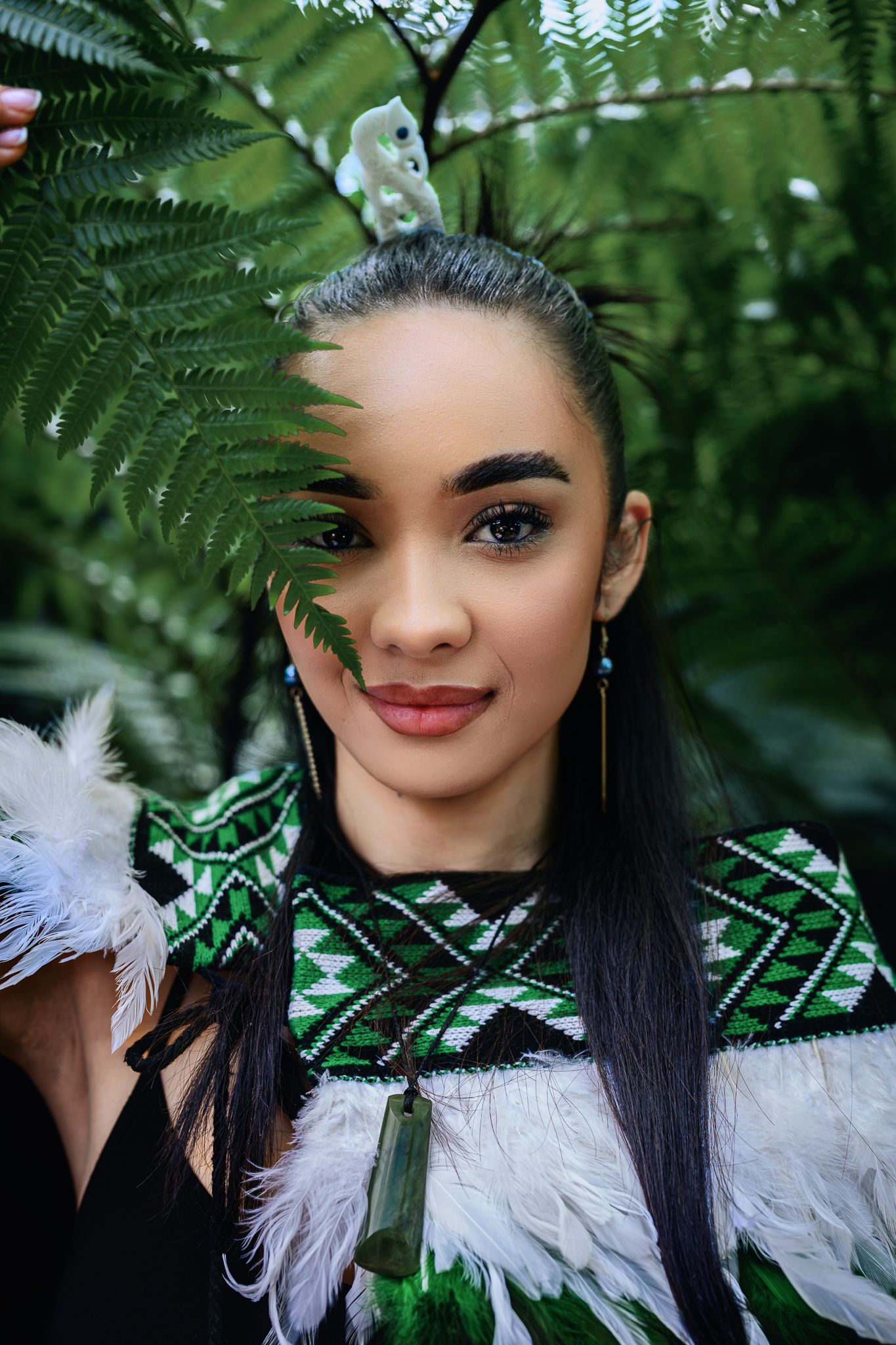 Young Maori woman in traditional taonga puoro necklace and feather cloak among native fern leaves.