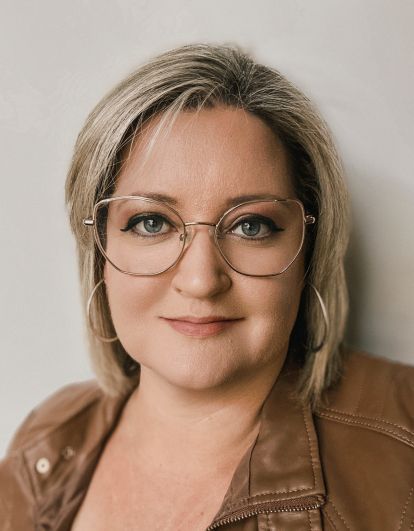 Close up portrait with glasses against neutral background wearing brown jacket.