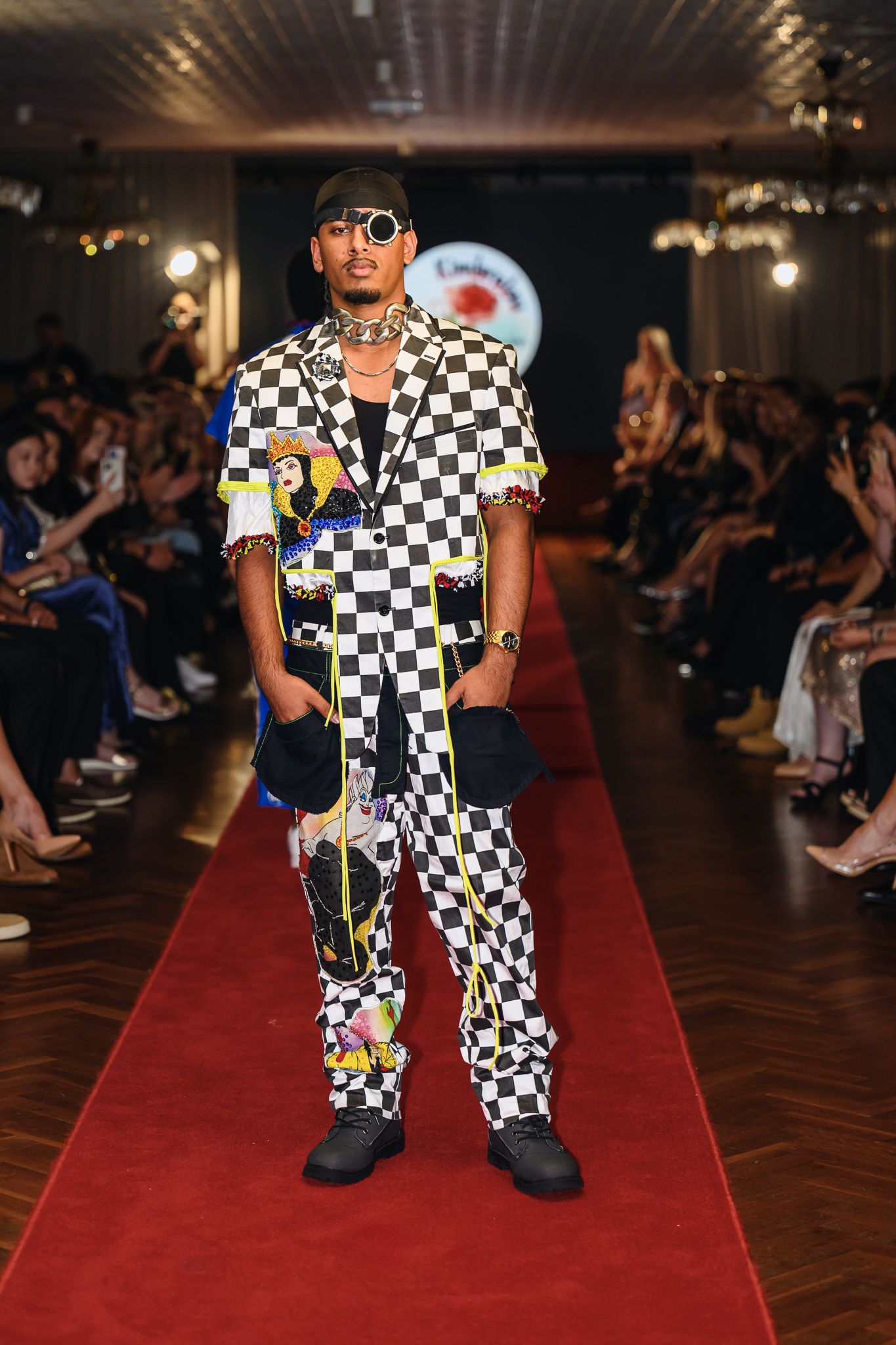Model showcases bold checkered pattern outfit on fashion show runway.