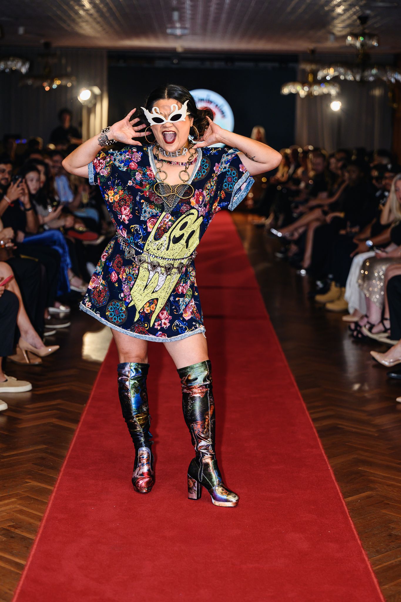 Model in floral dress and metallic boots strikes dramatic pose on fashion runway.