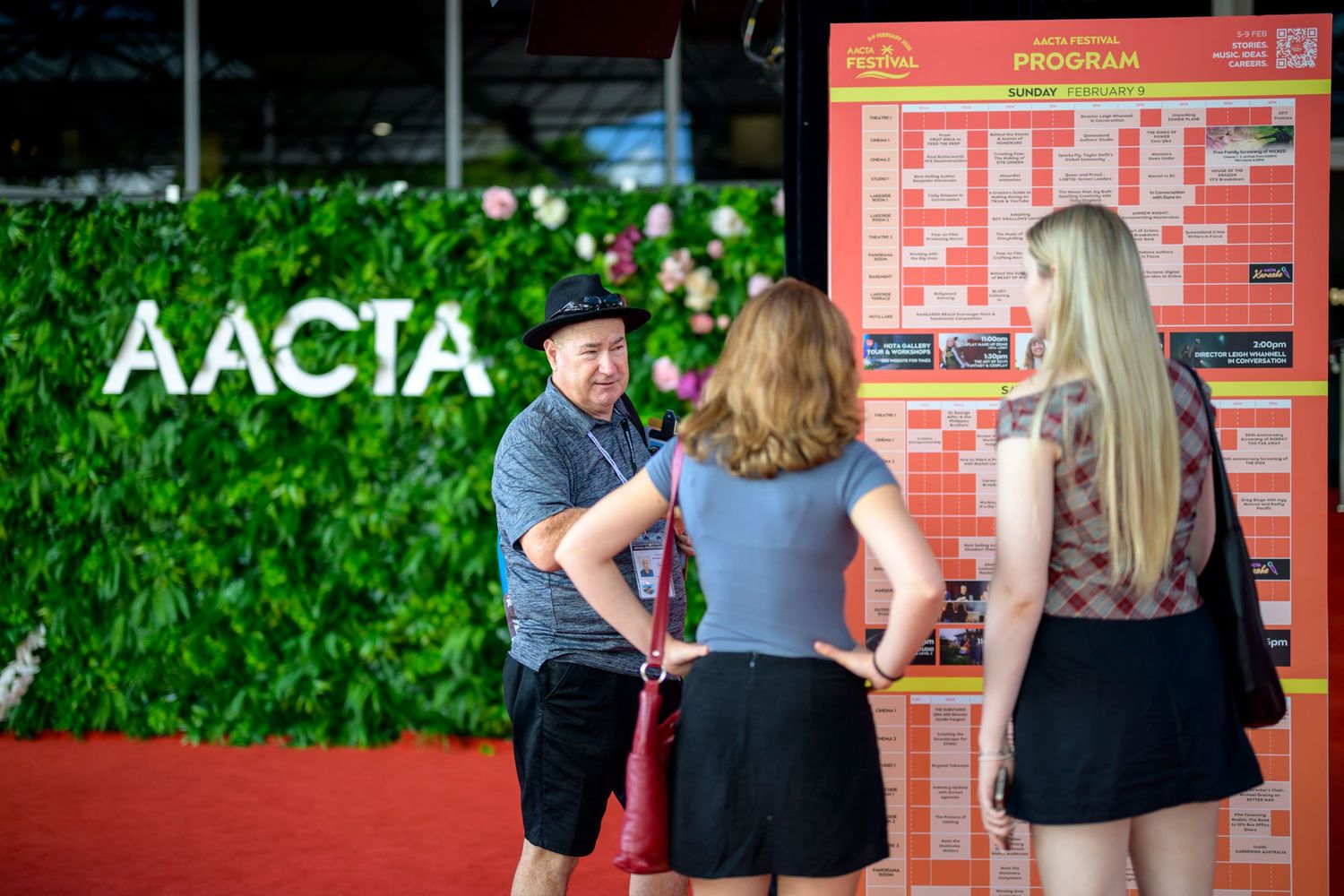 People gathered around program board at AACTA event discussing schedule.