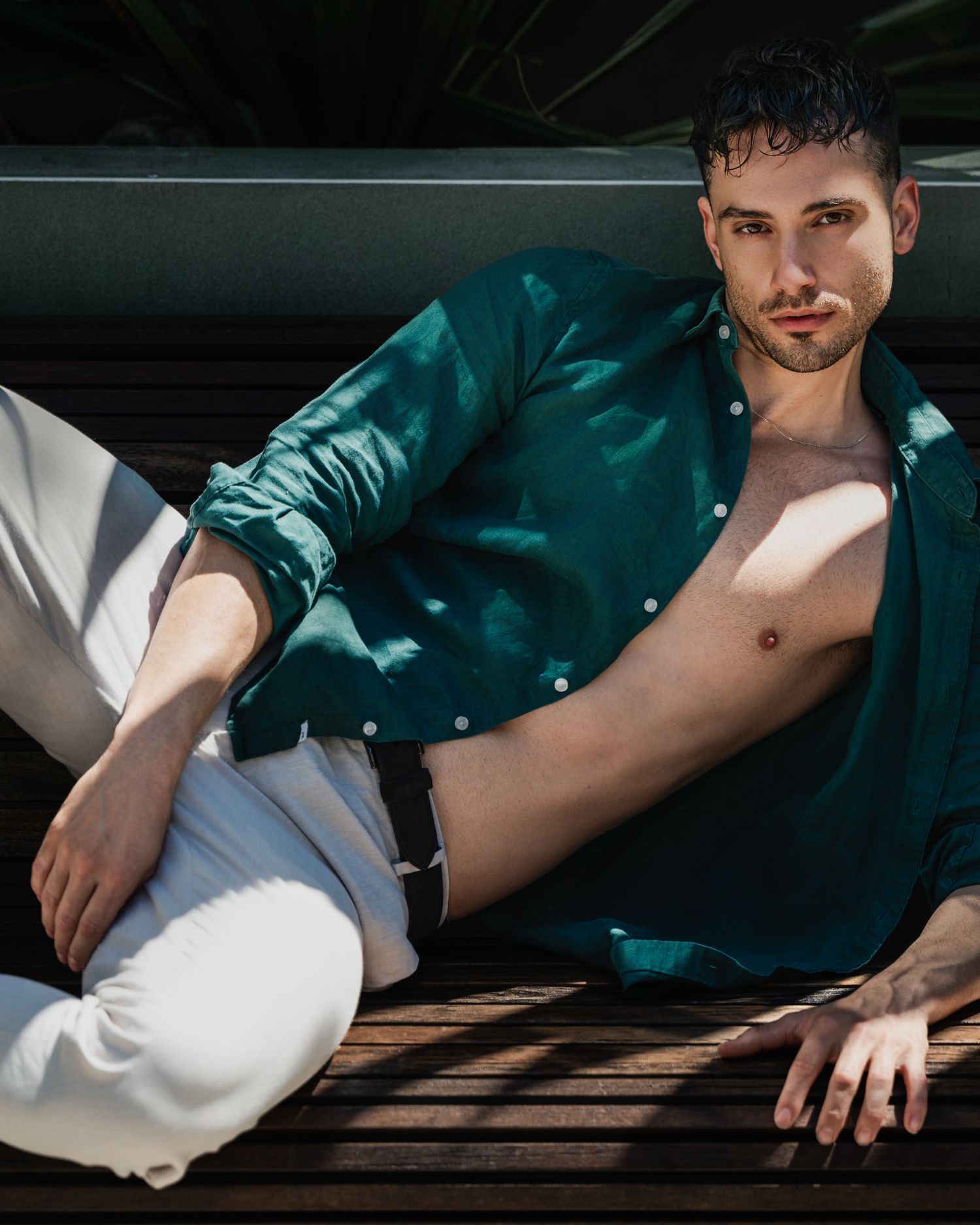 Fashion portrait of model in emerald silk shirt and white pants with dramatic lighting.