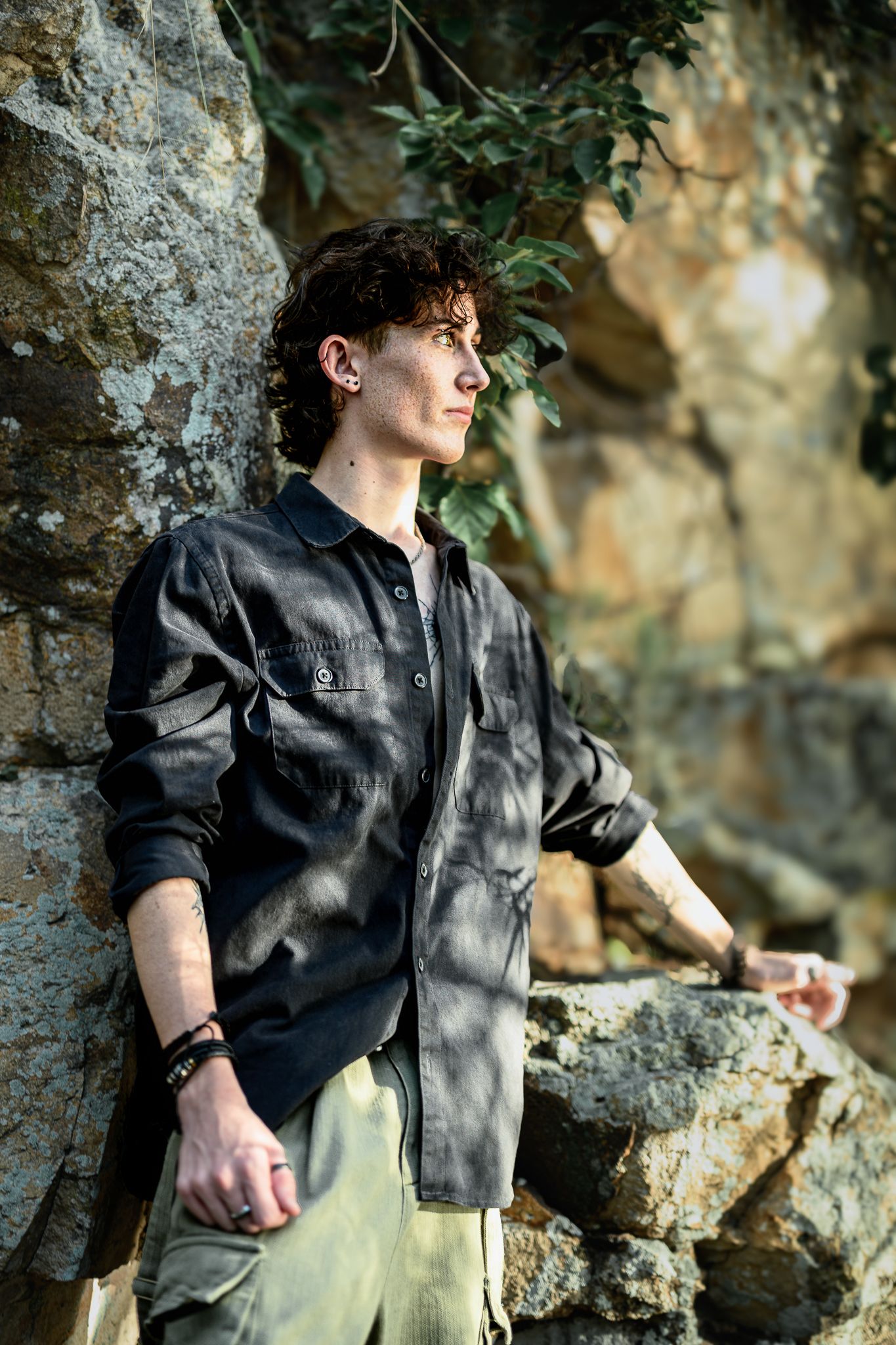 Casual fashion portrait against rocky wall wearing black button-up shirt.