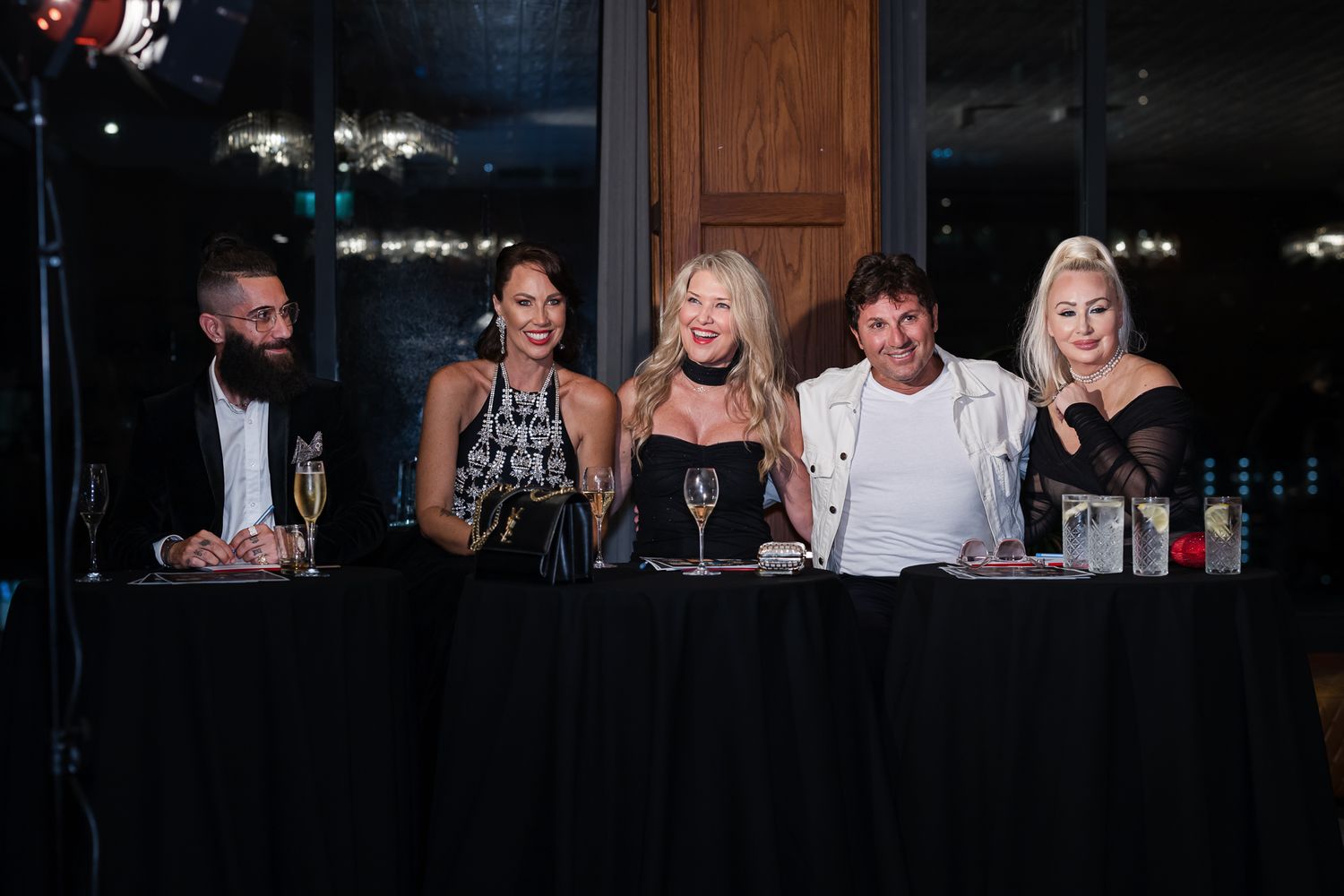 Five people sit at a panel table draped in black cloth during an evening event.