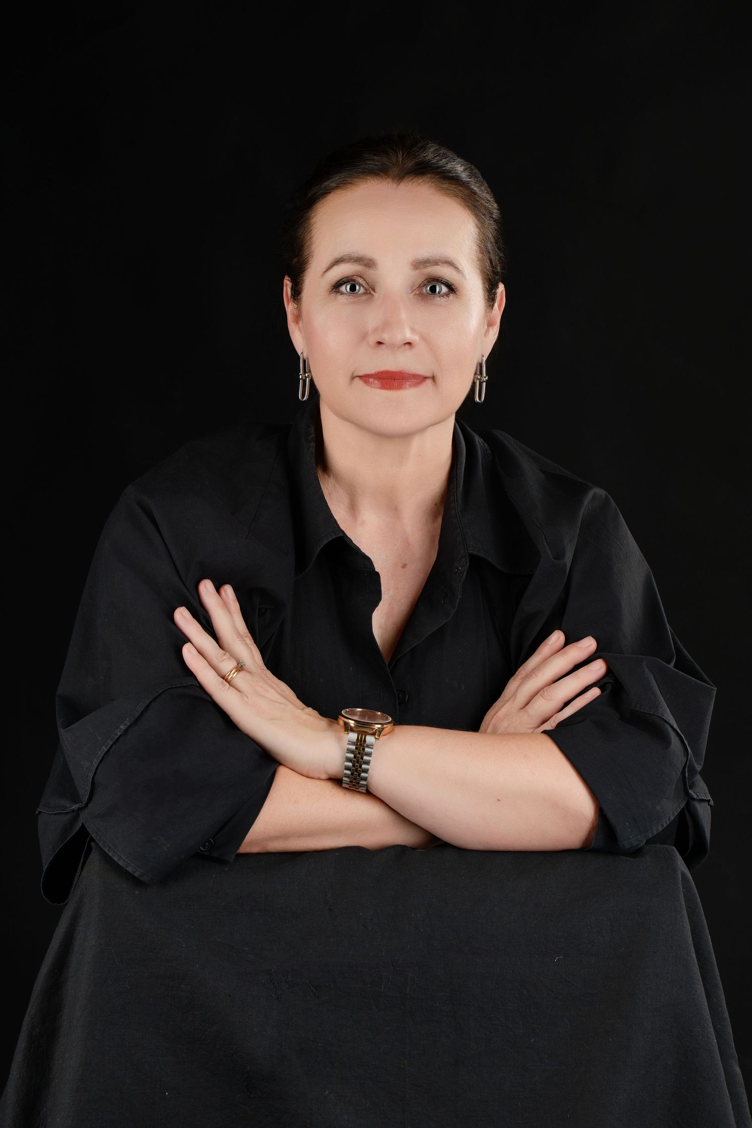 Studio portrait of a person in black with crossed arms against dark background.