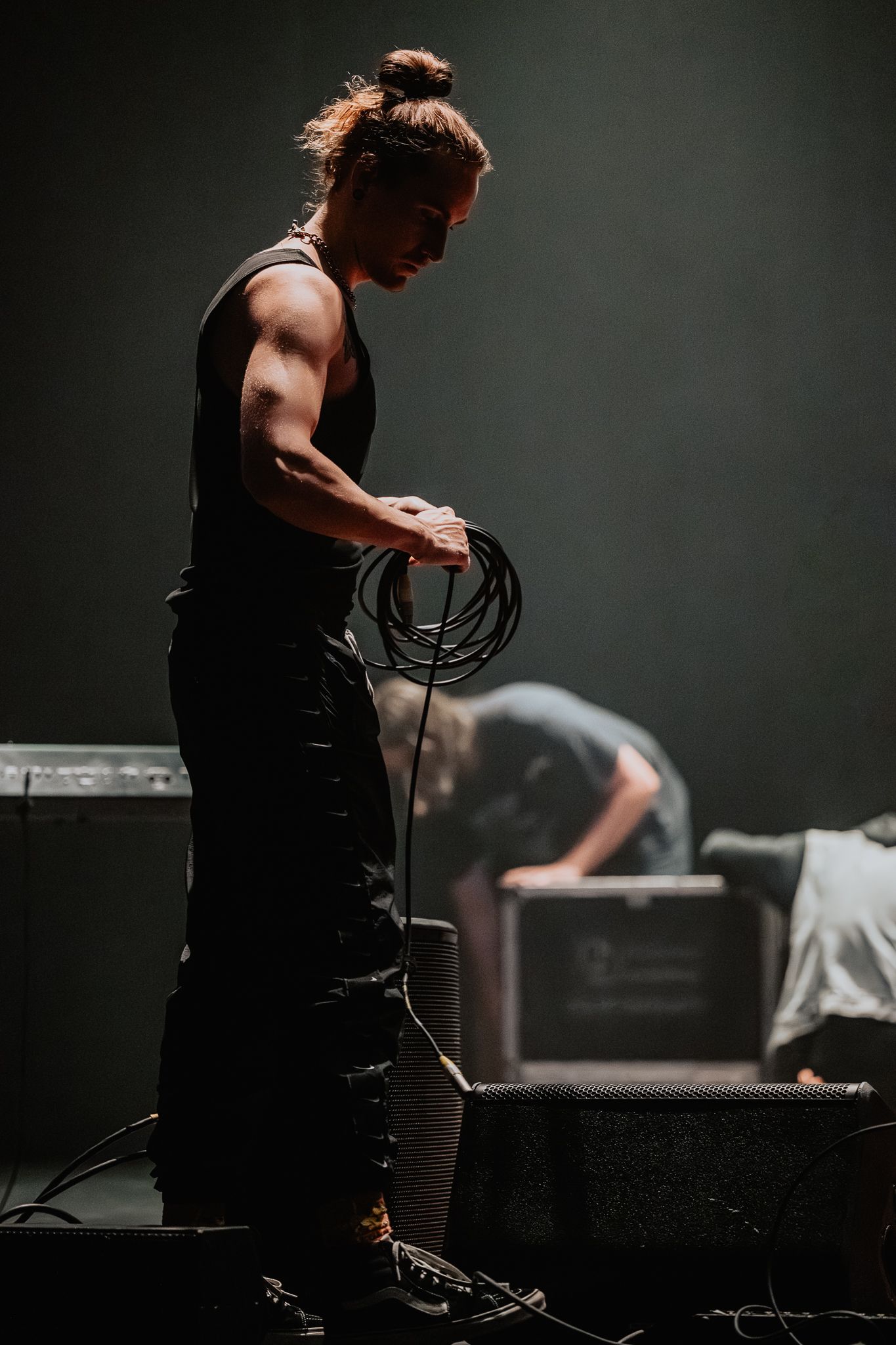 Musician performing on stage in dark lighting with electronic equipment and cables.