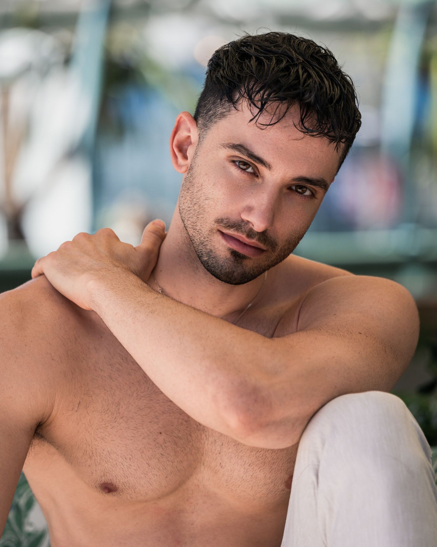 Athletic man posing shirtless against blurred outdoor background.