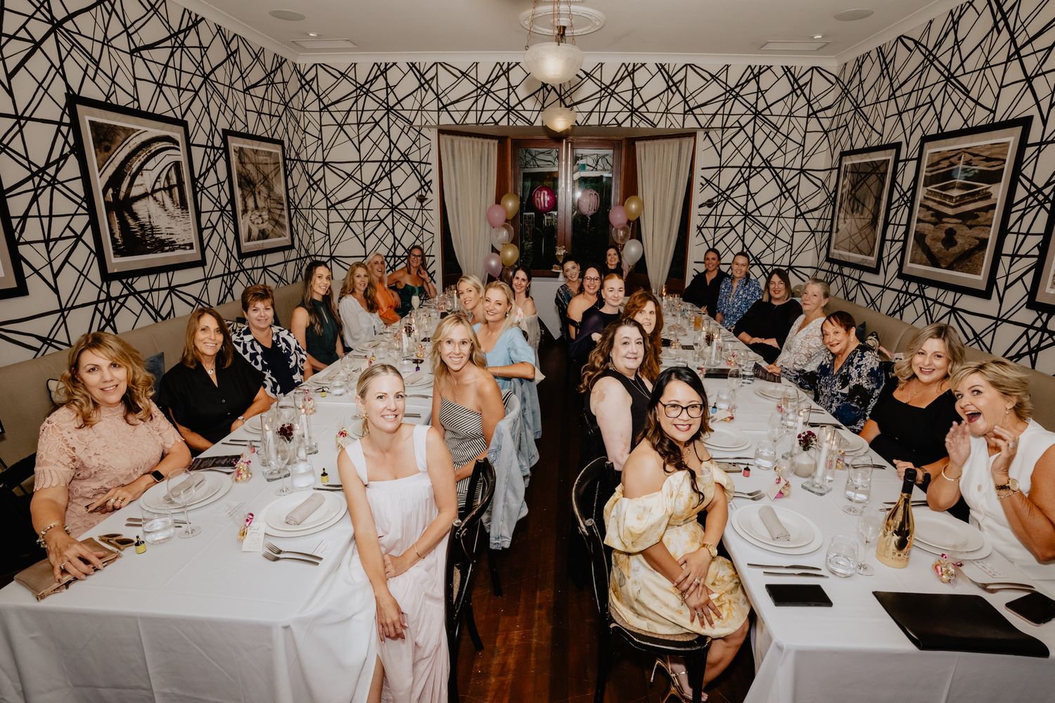 Wedding reception dining room with geometric wallpaper and guests seated at white-clothed tables.