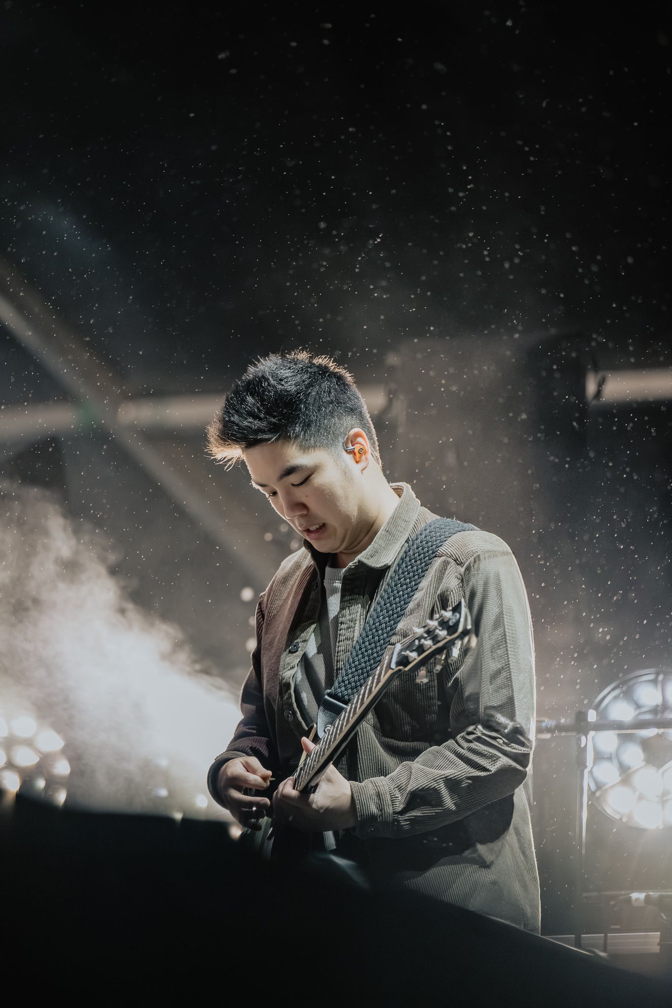 Guitarist performing on stage with moody lighting and fog effects.