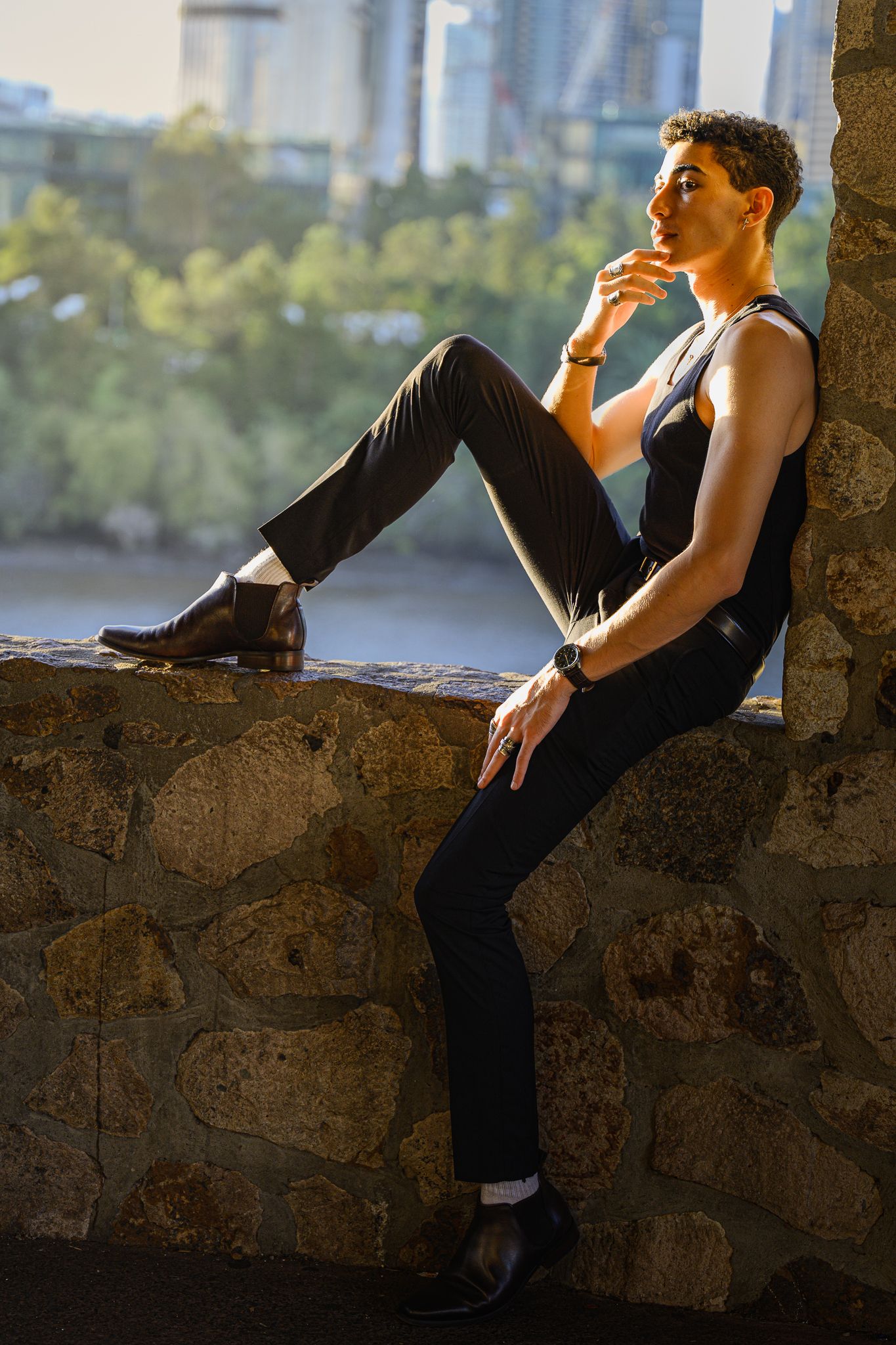 Artistic portrait of performer in black attire reclining on stone ledge.