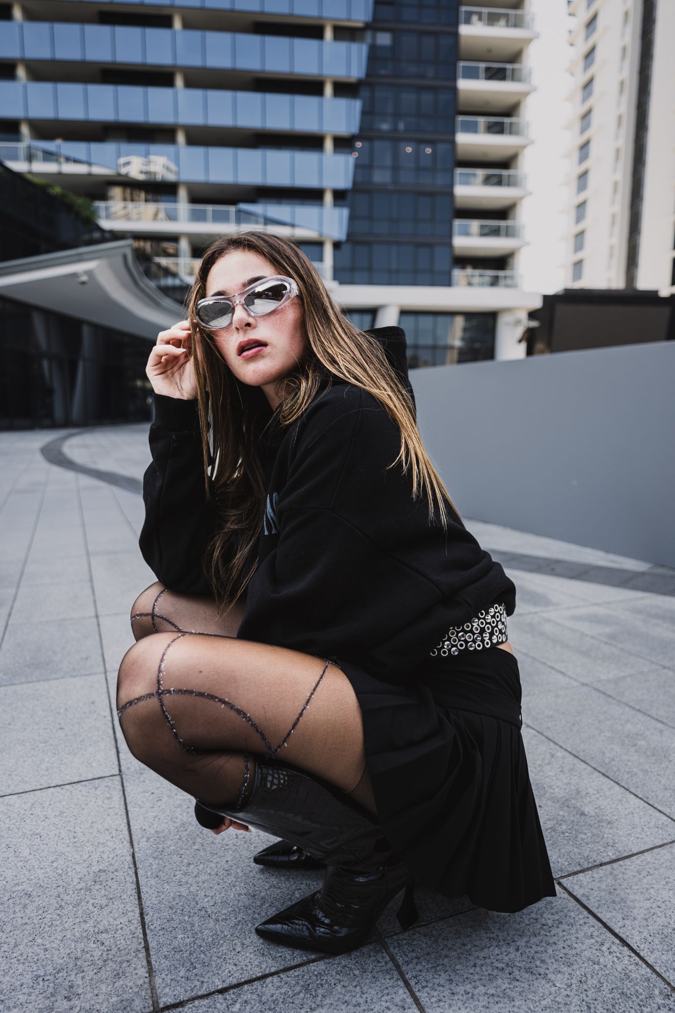 Person in black outfit crouching on urban rooftop or terrace.