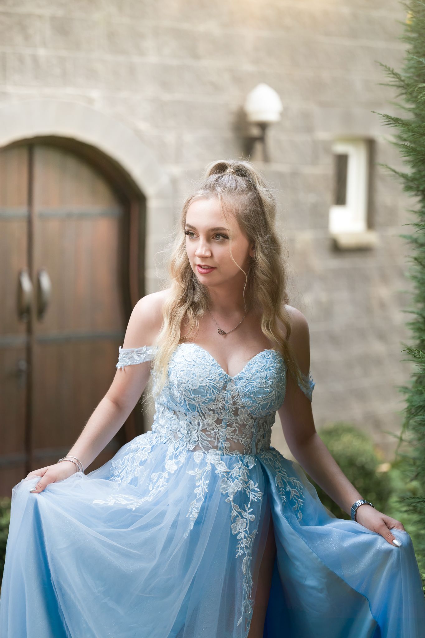 Elegant blue formal dress with lace details photographed against stone wall architecture.
