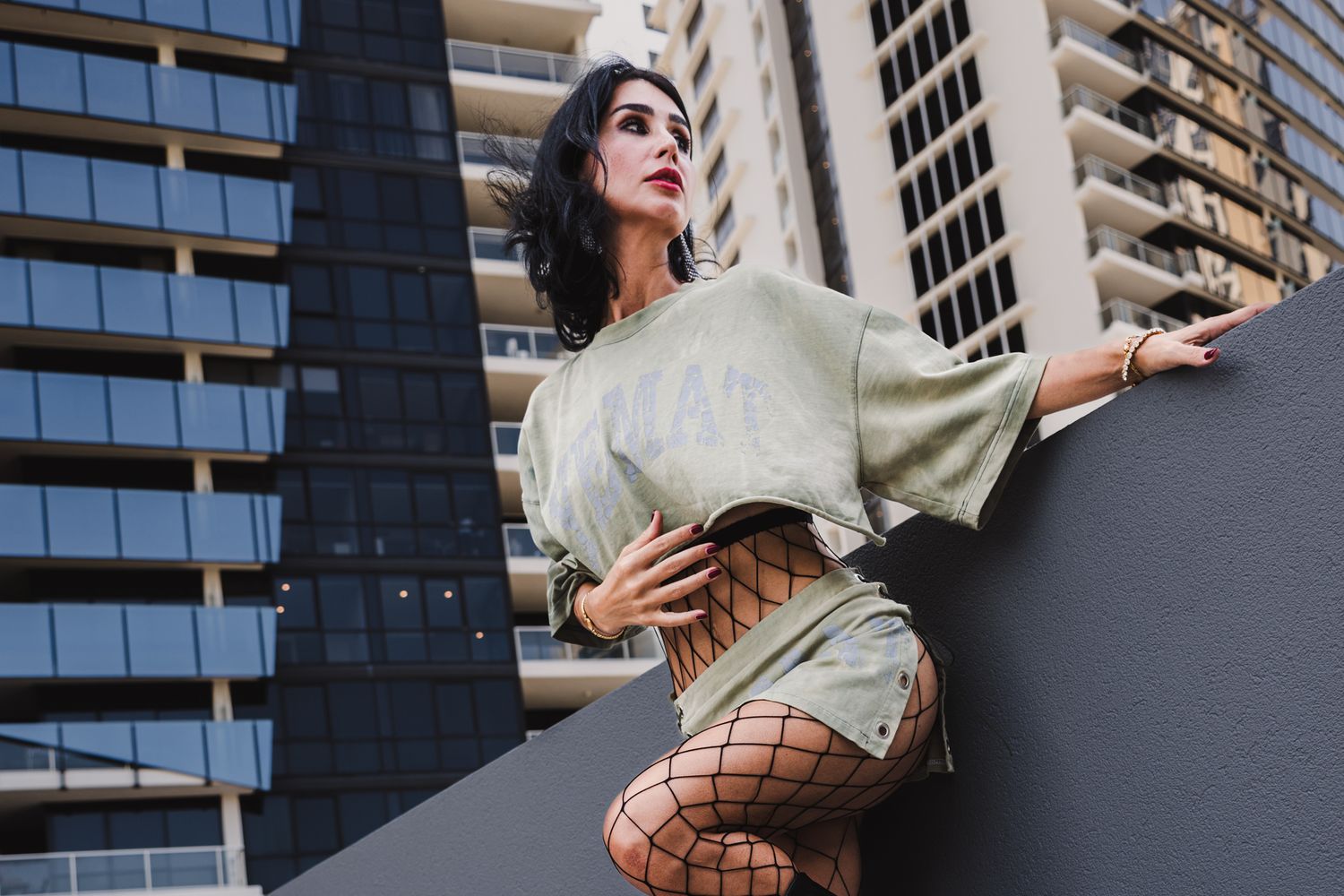 Street style portrait with oversized sweater and fishnet tights against modern architecture.