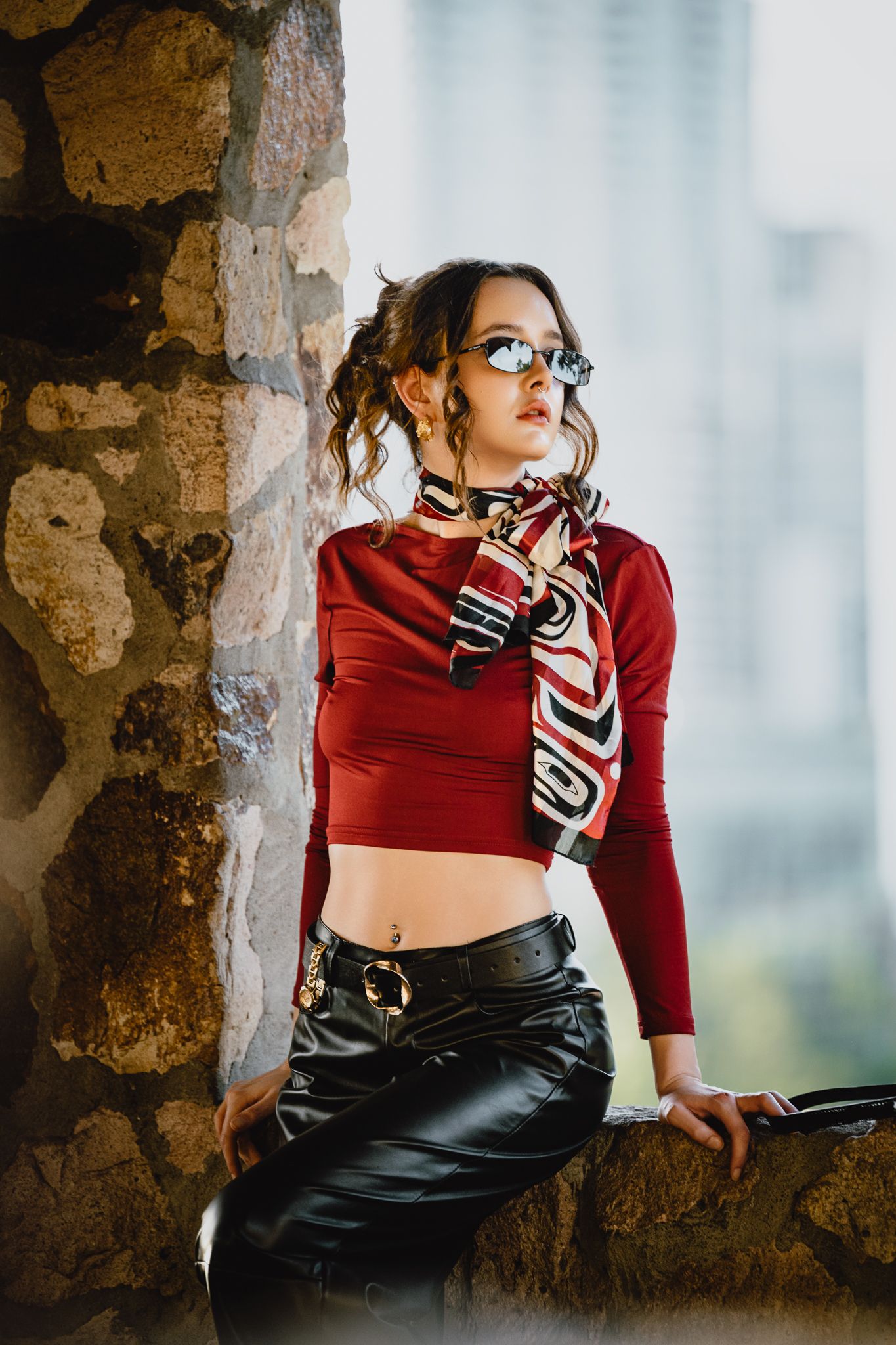 Fashion portrait featuring red crop top and leather pants against city view.