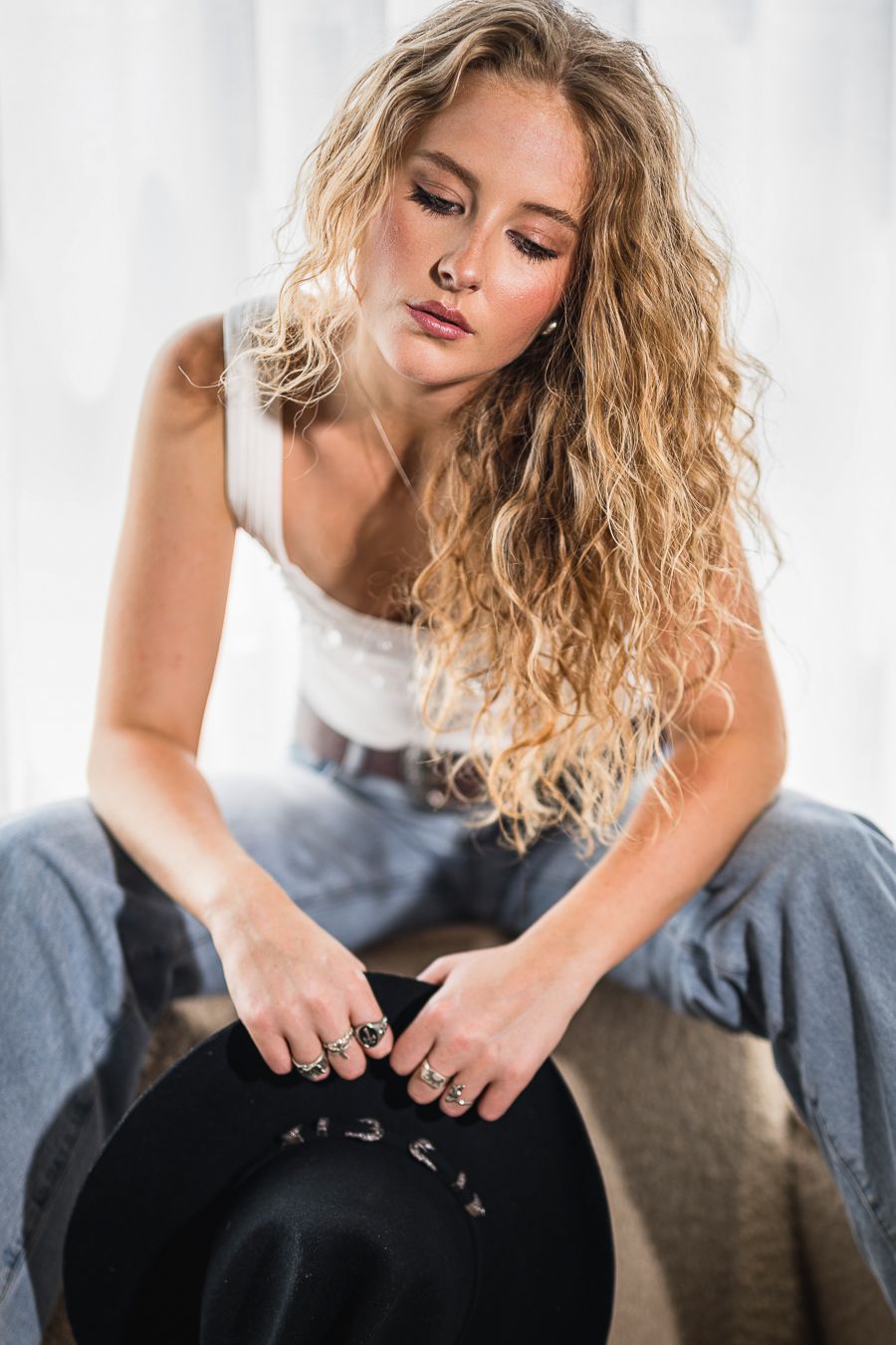 Artistic portrait with curly blonde hair and black hat holding pose in casual attire.
