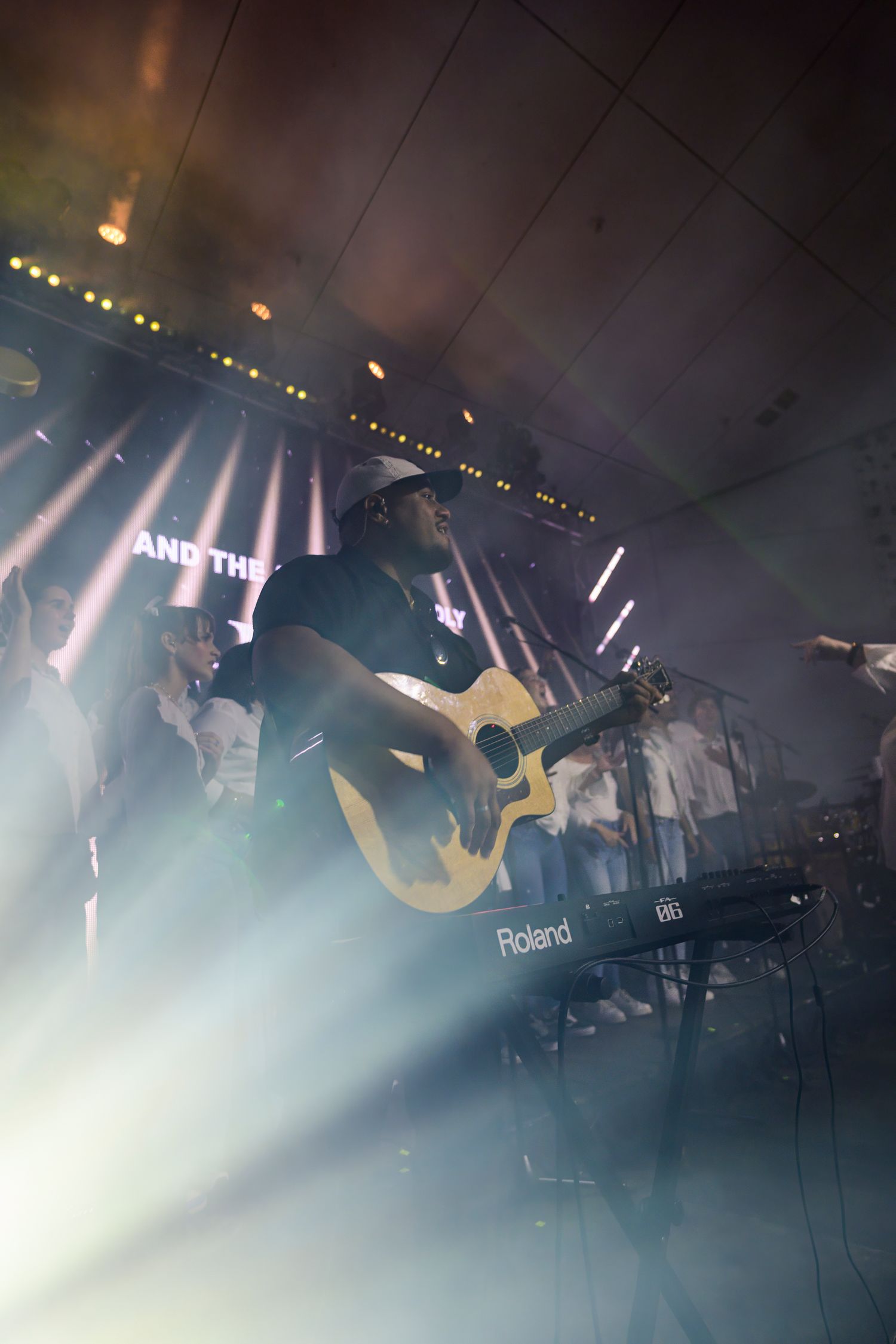Musician playing acoustic guitar on stage with dramatic lighting and smoke effects.