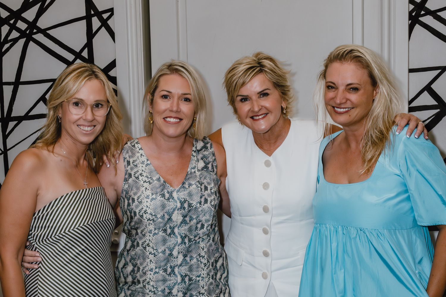 Group of women in summer dresses posing together against geometric patterned wall.