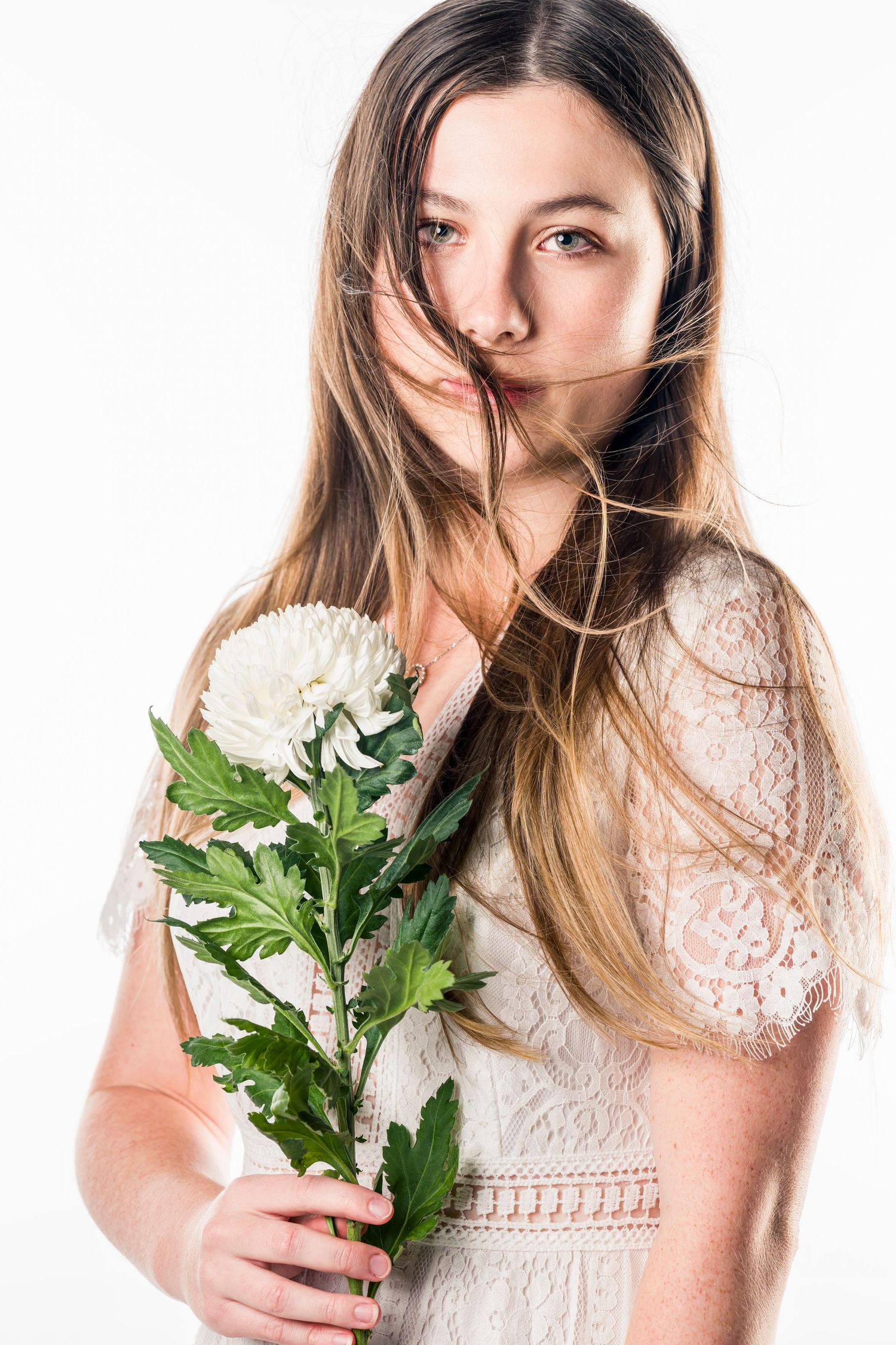 Portrait with white flowers wearing romantic lace dress against white backdrop.