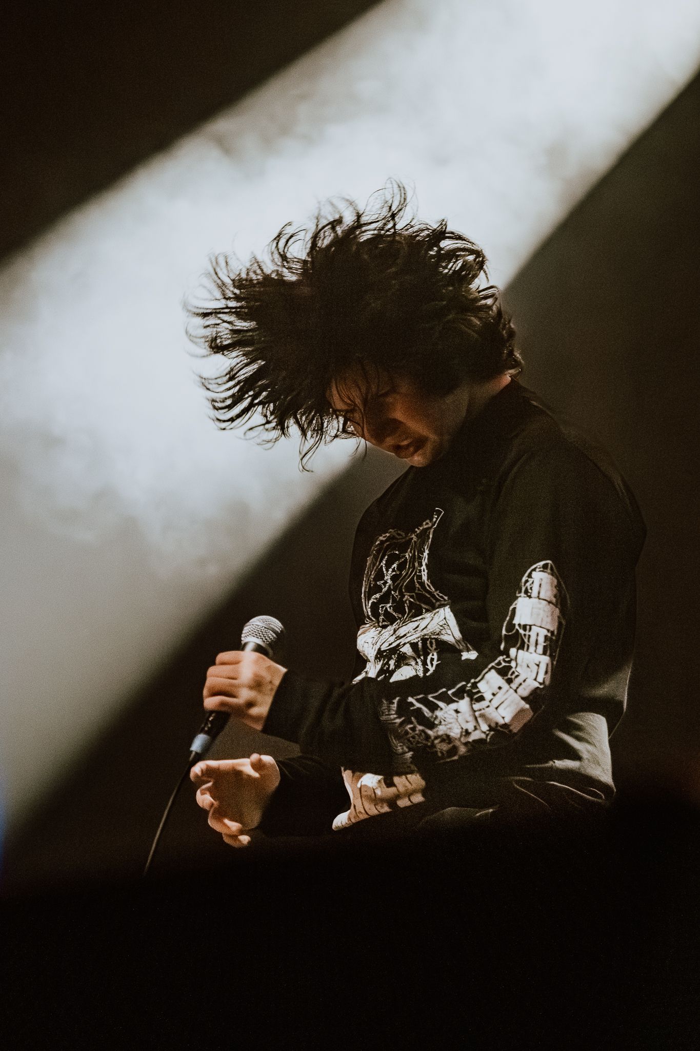 Dynamic performance shot with hair motion captured against white spotlight background.