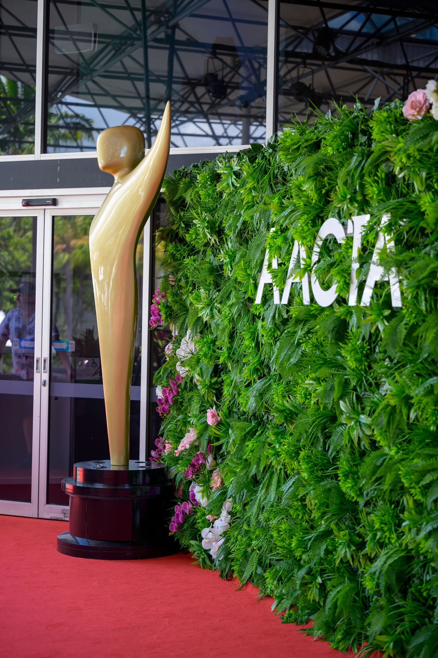 Golden statue award displayed next to green foliage wall with white text.