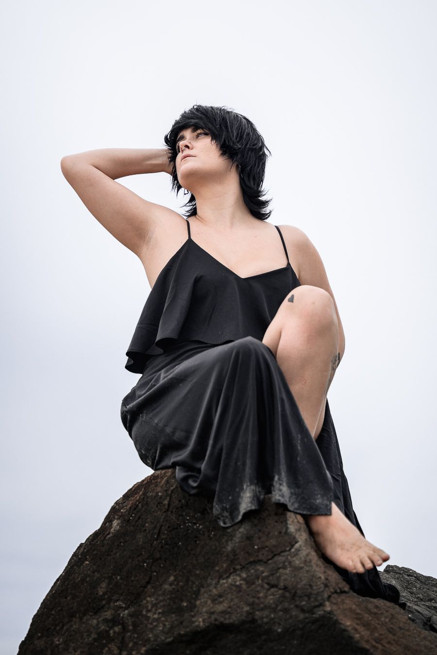 Figure in black flowing dress poses dramatically on dark stone surface.