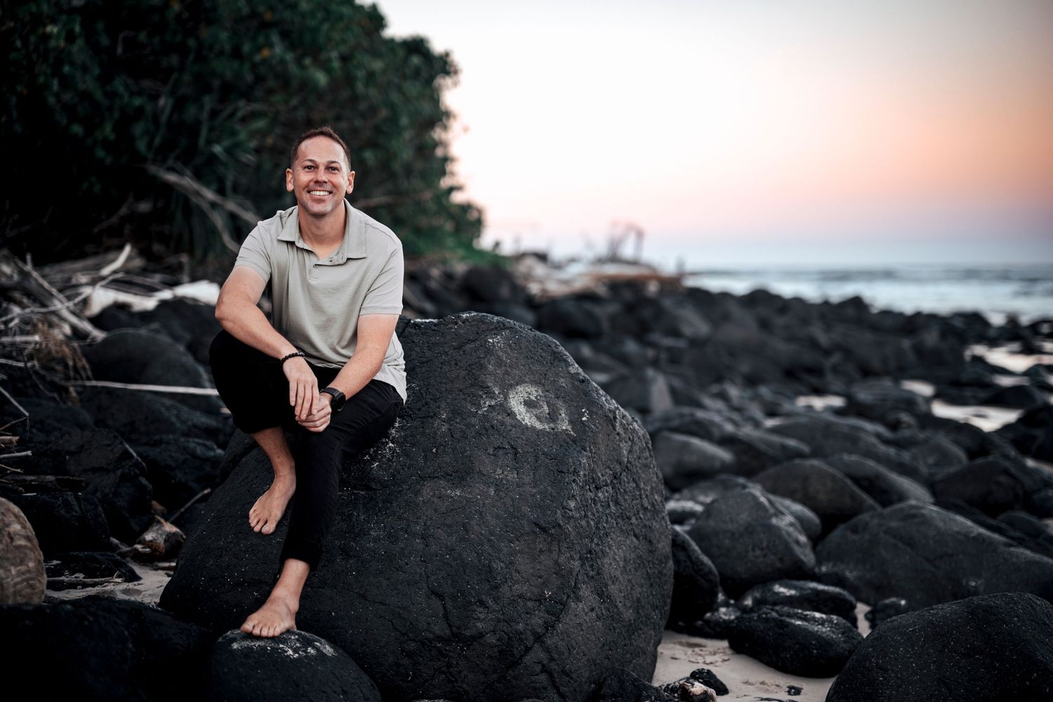 Person sitting on black volcanic rocks at beach during sunset.