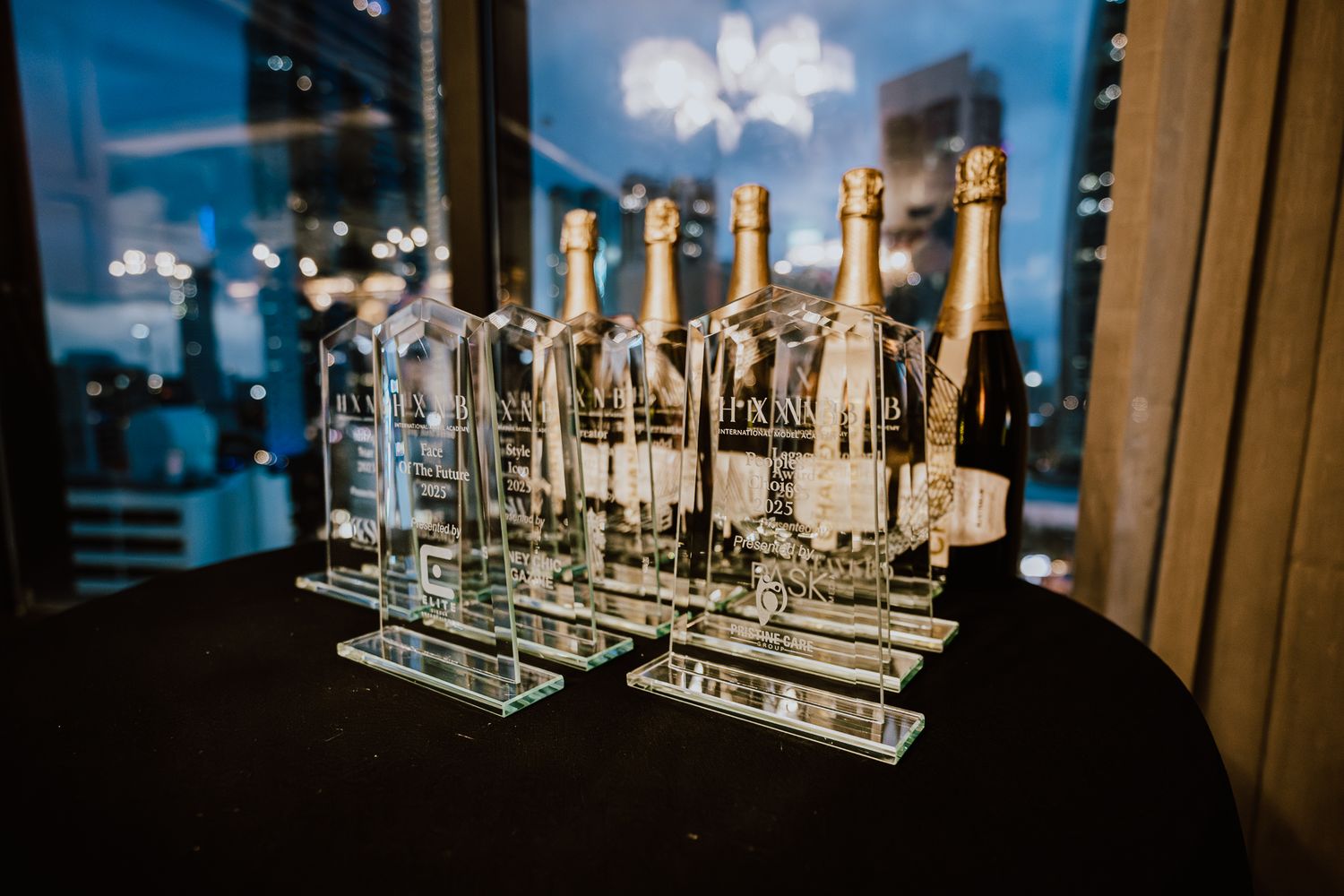 Row of transparent glass trophy awards displayed on dark surface with blue ambient lighting.