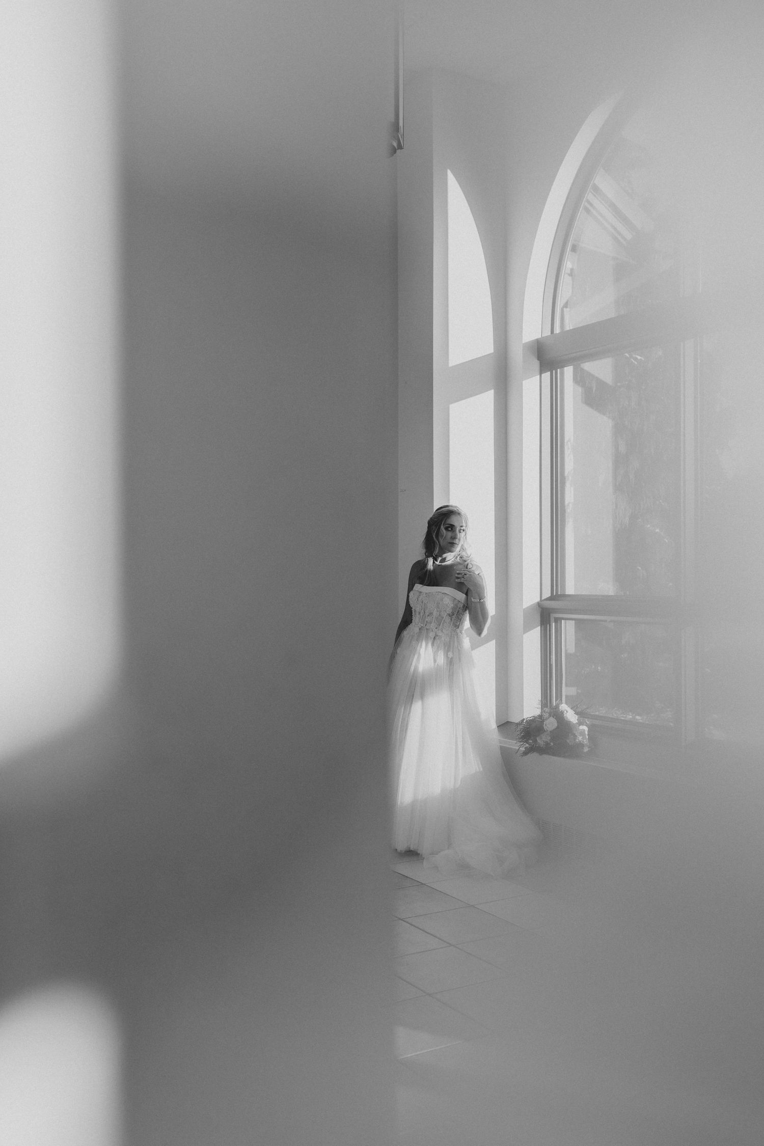 A series of ethereal black and white photos showing a figure in a white dress standing near windows in a bright room.