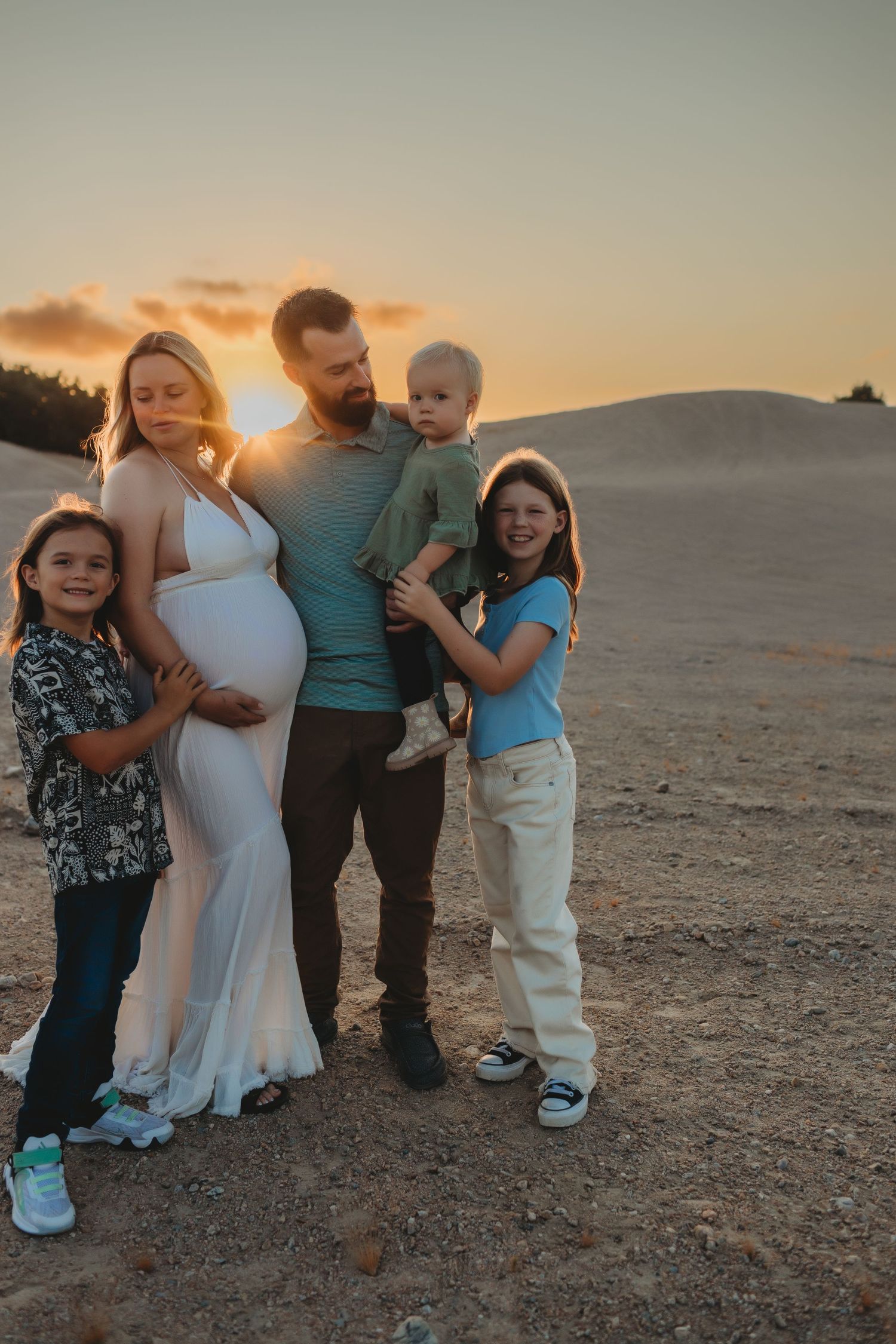 Family stands together on desert terrain against a warm sunset sky creating intimate silhouettes.