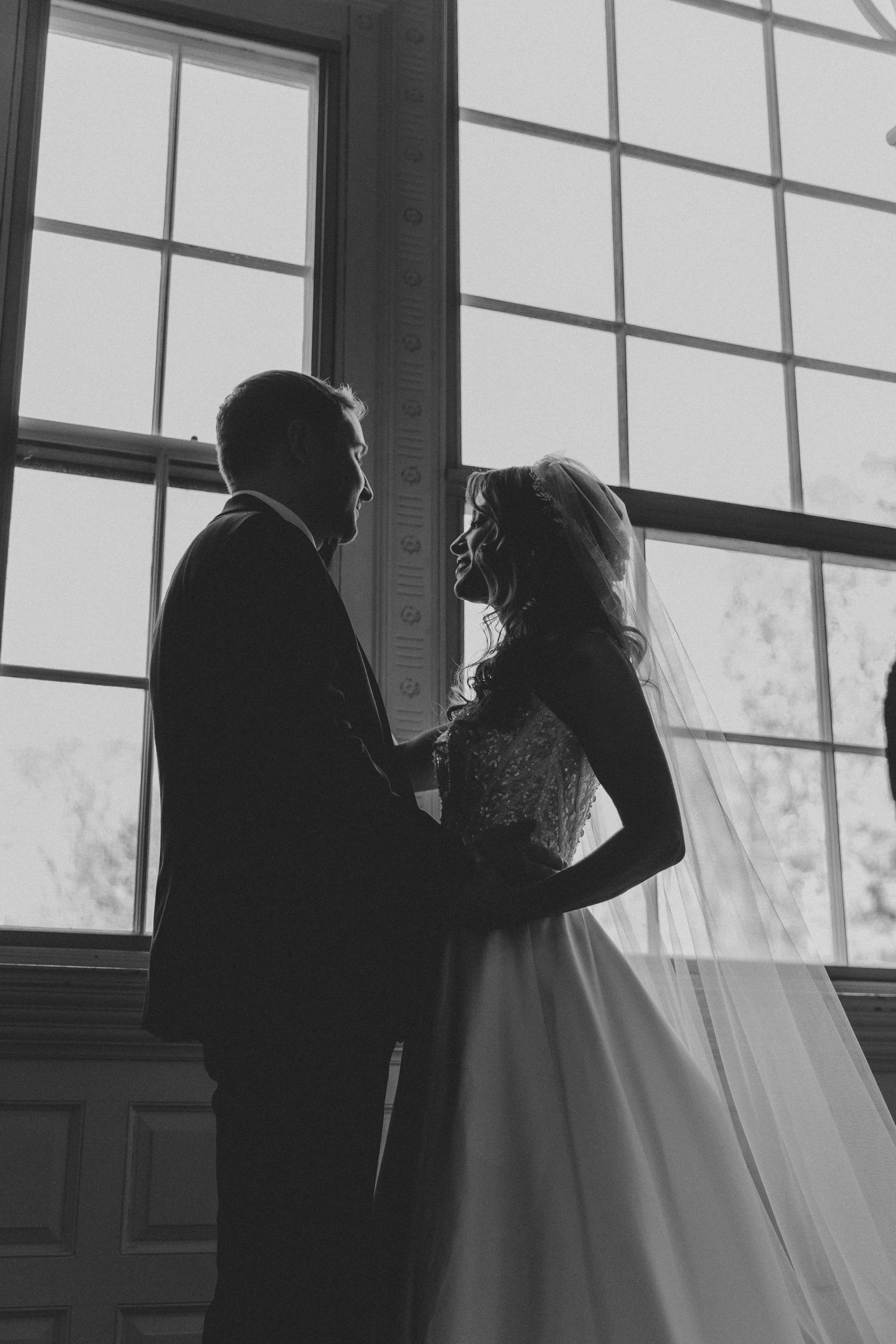A romantic silhouette of a couple sharing an intimate moment against a bright window in black and white photography.