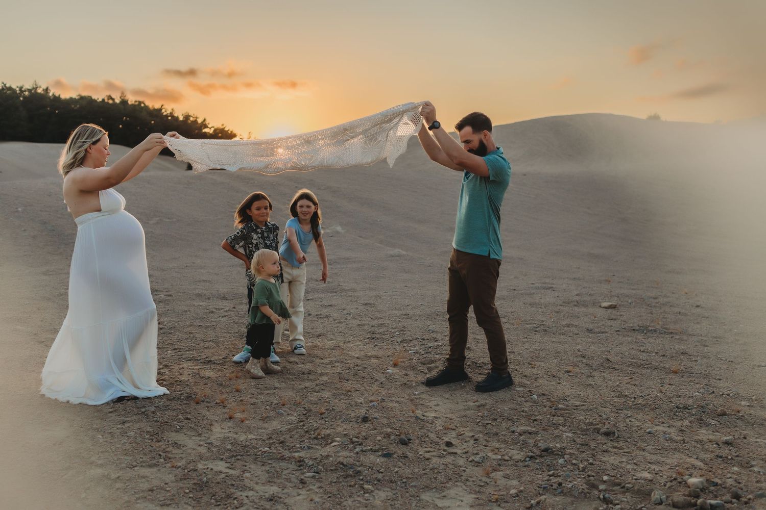 A romantic sunset photoshoot on a sandy beach with people posing and dancing in the golden light.